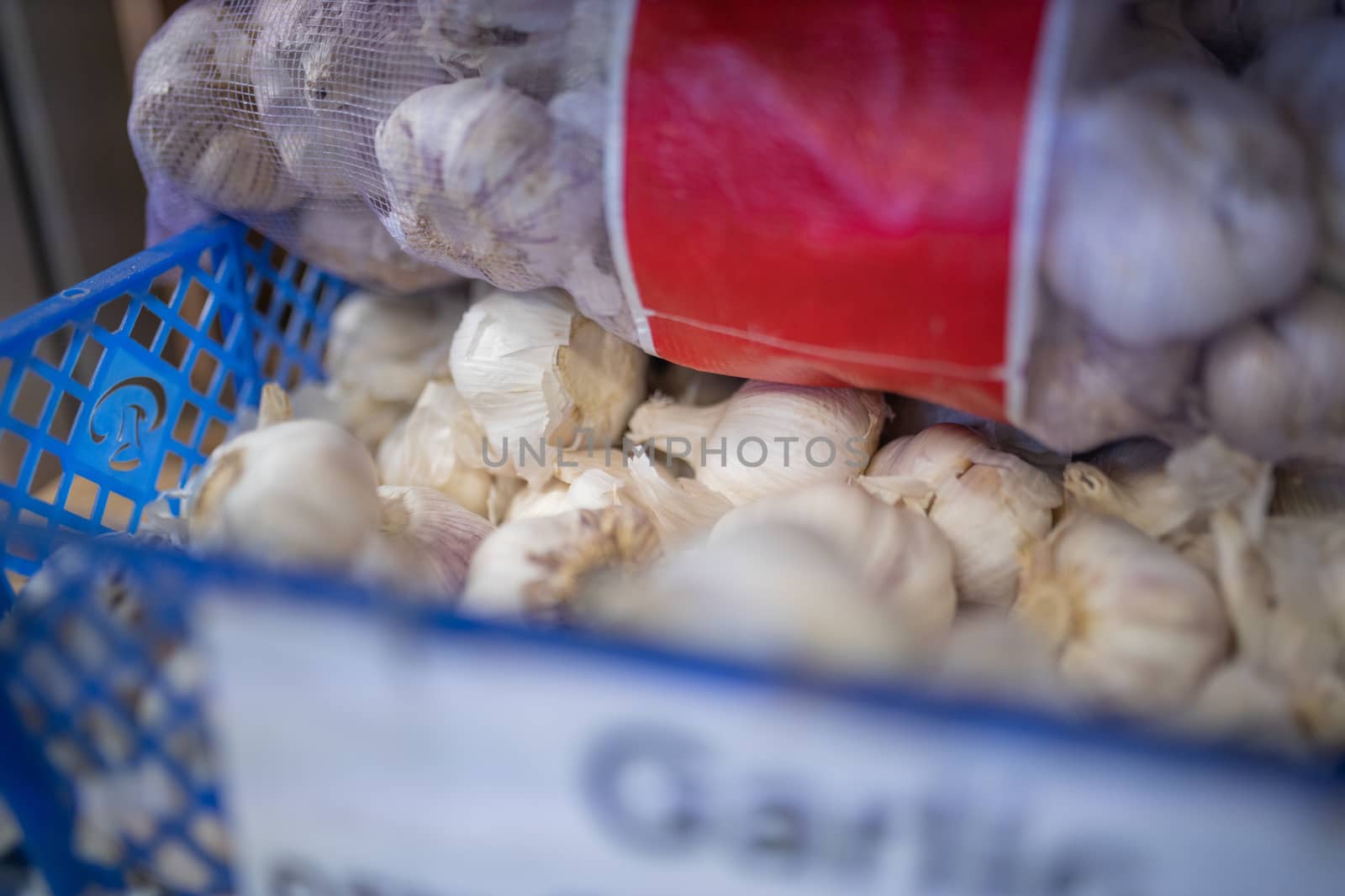 Picture of the word Garlic Written on a blurry Sign on a Blue Plastic Basket Full of Garlic