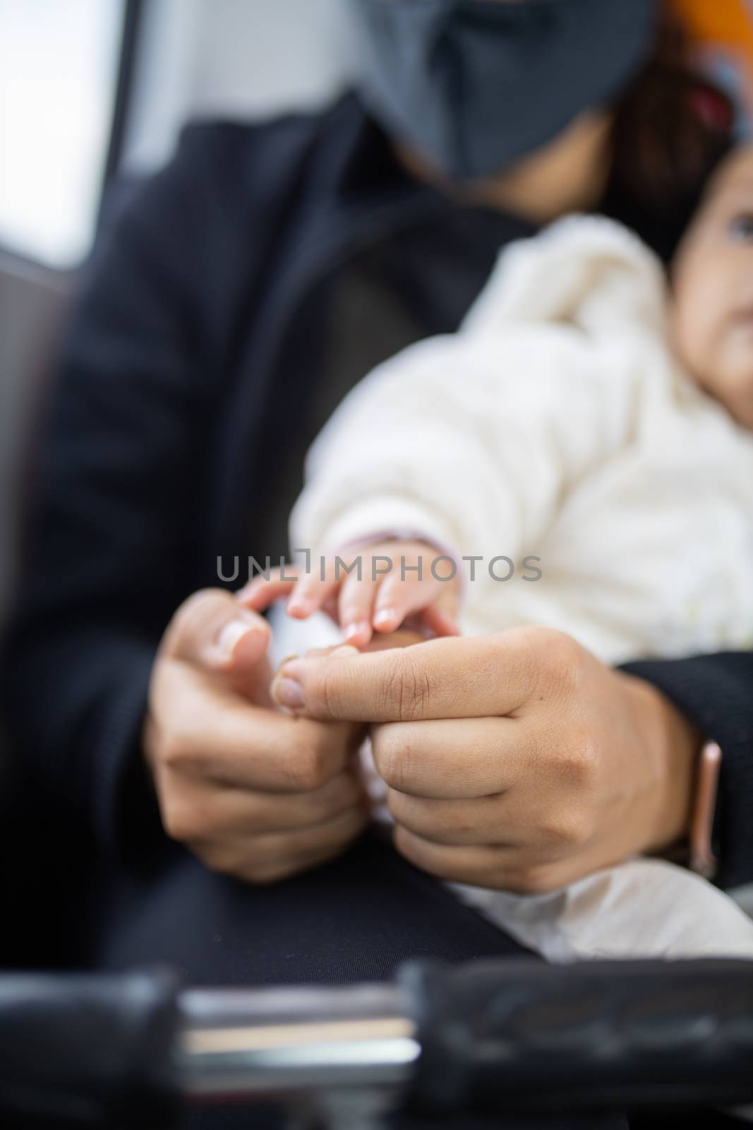 Little hand of a baby reaching the hands of her mother who is holding her as she sits next to a window