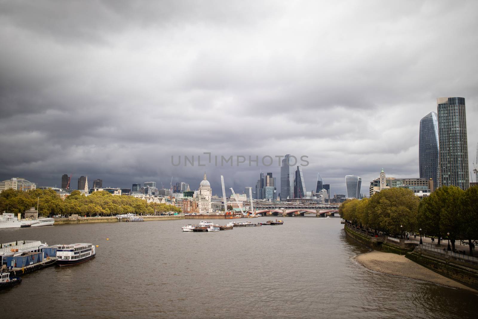 Landscape picture of the River Thames surrounded by trees and with a cloudy skyline and cityscape from London, UK as the background