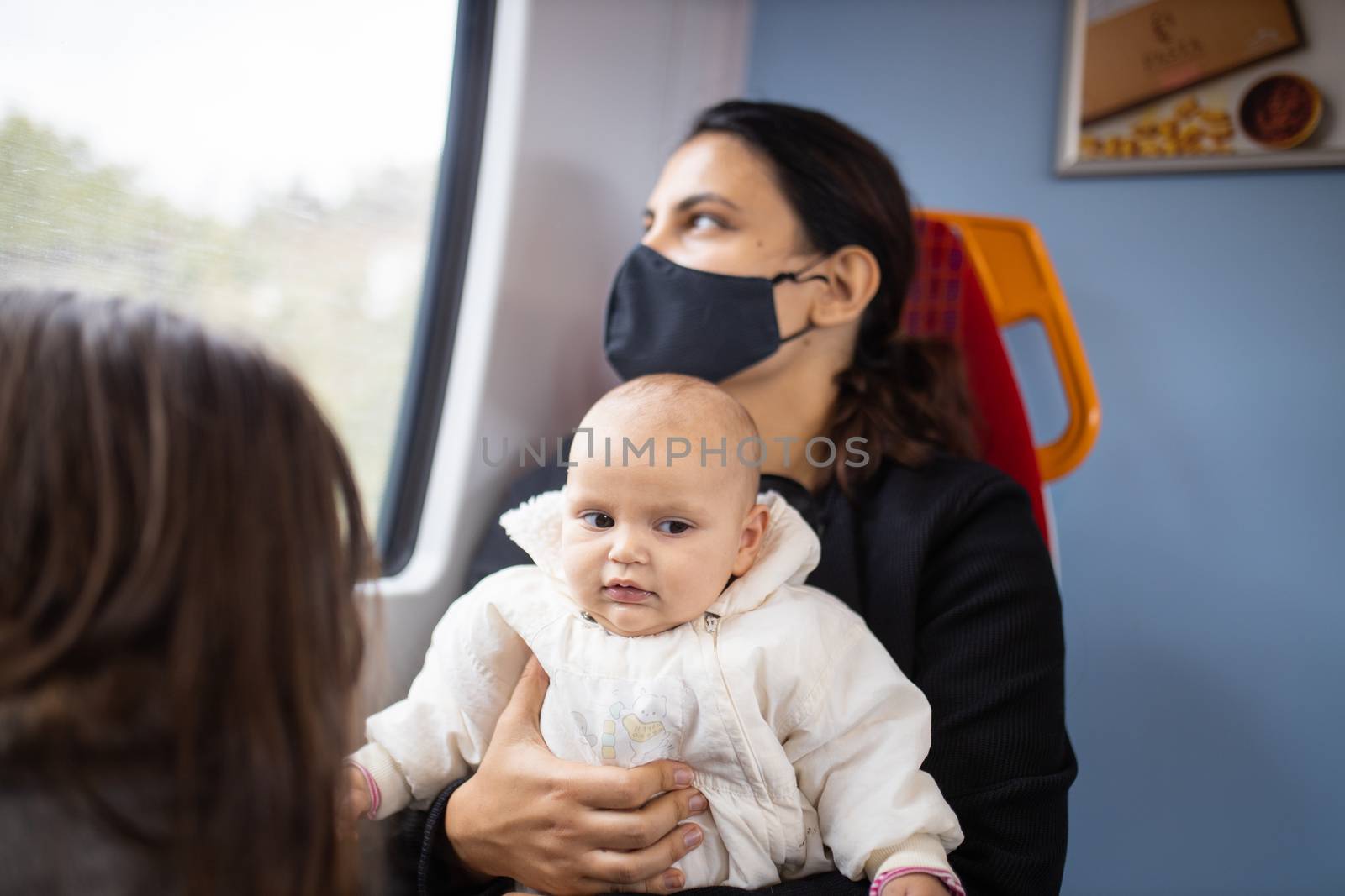 Woman wearing a face mask and looking through the window of a bus as she holds her smiling baby in her arms