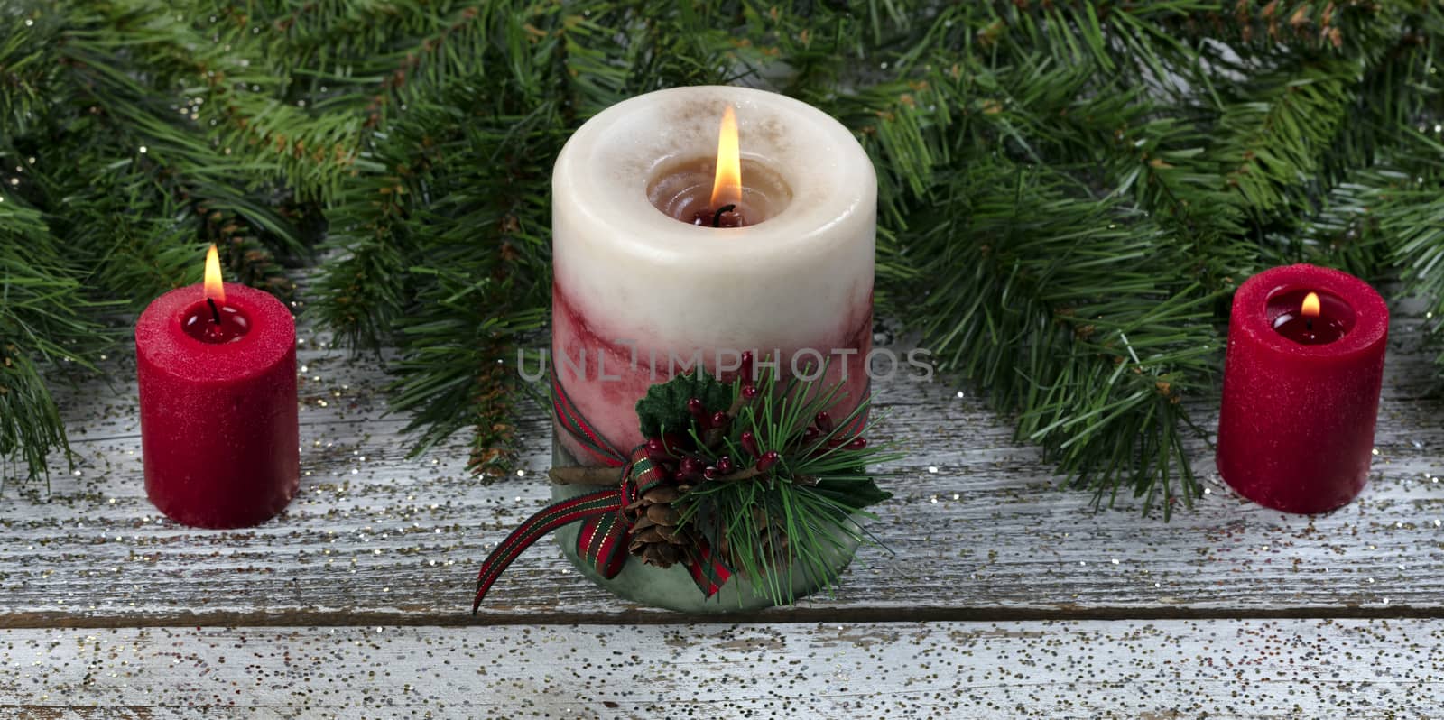Close up of a large glowing candle surrounded with other Christmas decorations 