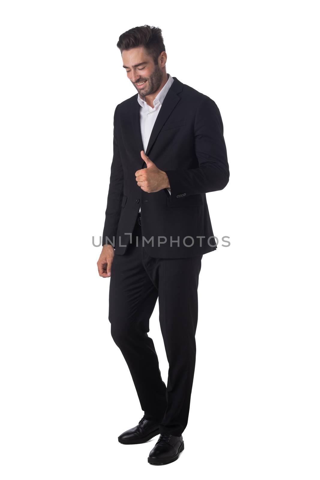 Full length portrait of young handsome business man in black suit smiling and showing thumbs up studio isolated on white background