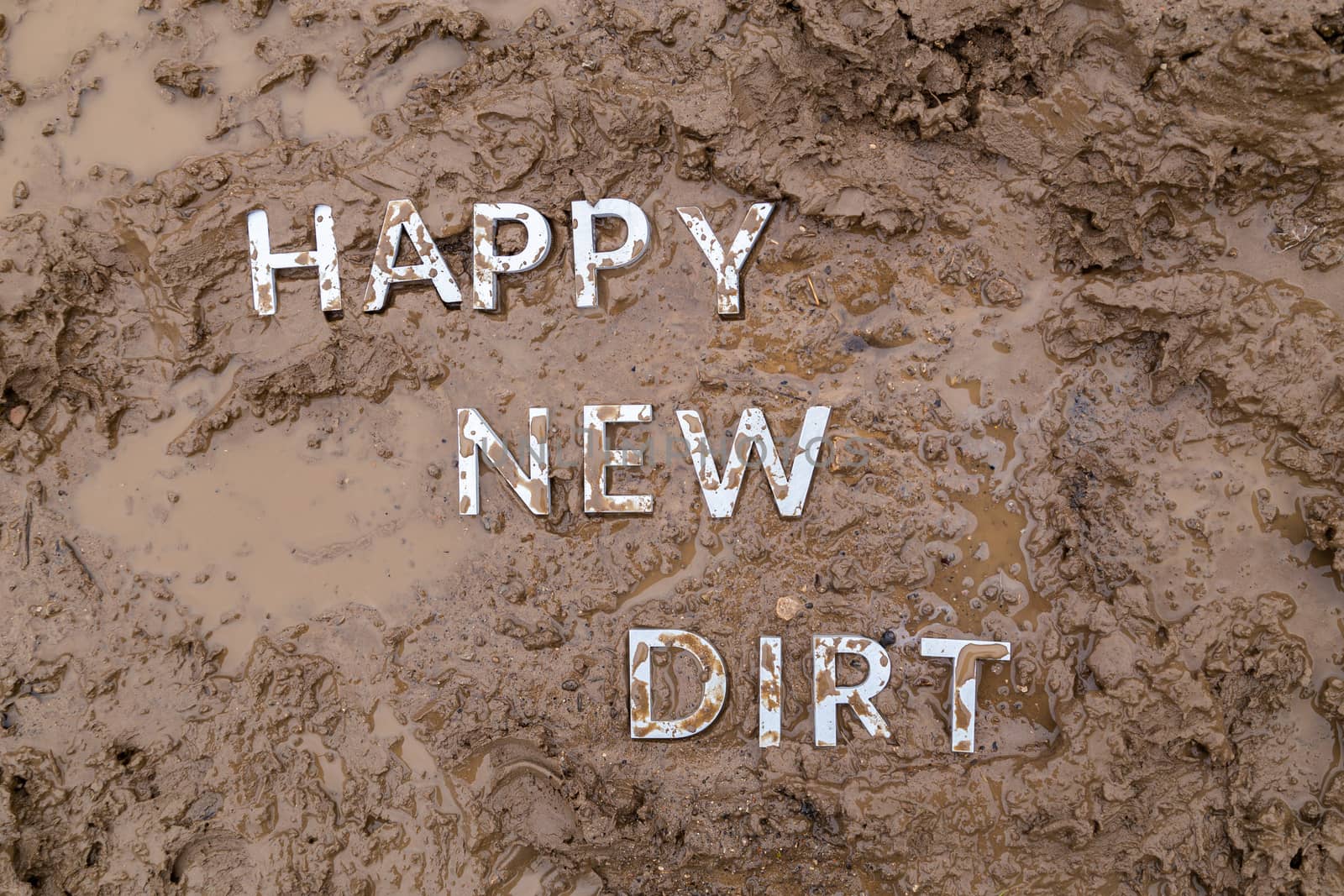 the words happy new dirt laid with silver metal letters on wet mud surface in directly above perspective under cloudy autumn day light