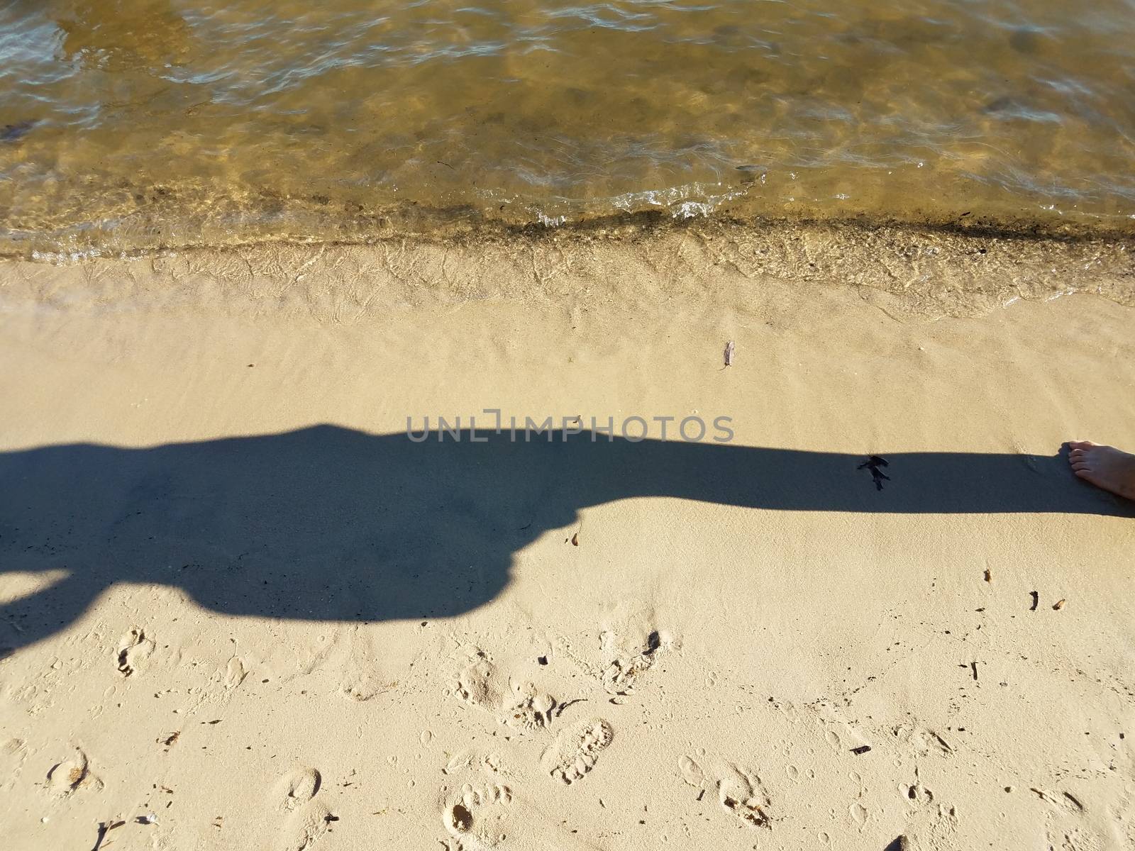 shadow of person on beach sand with water by stockphotofan1