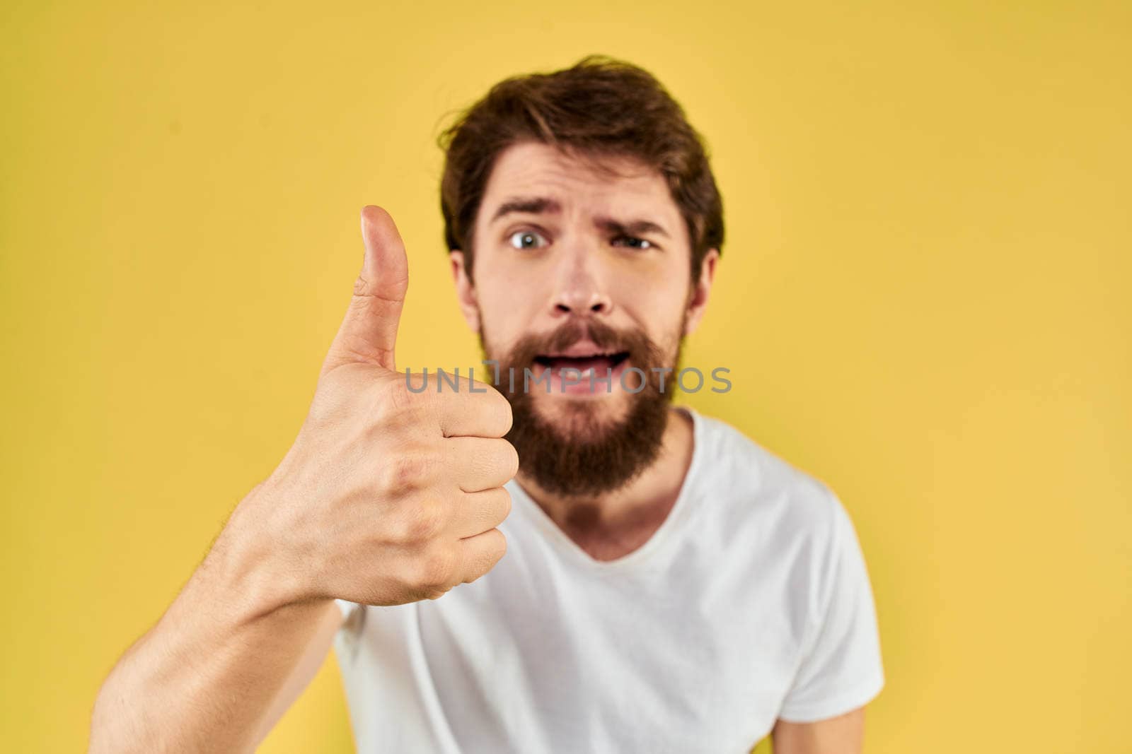 Bearded man emotions fun gesture with hands white t-shirt close-up yellow background. High quality photo