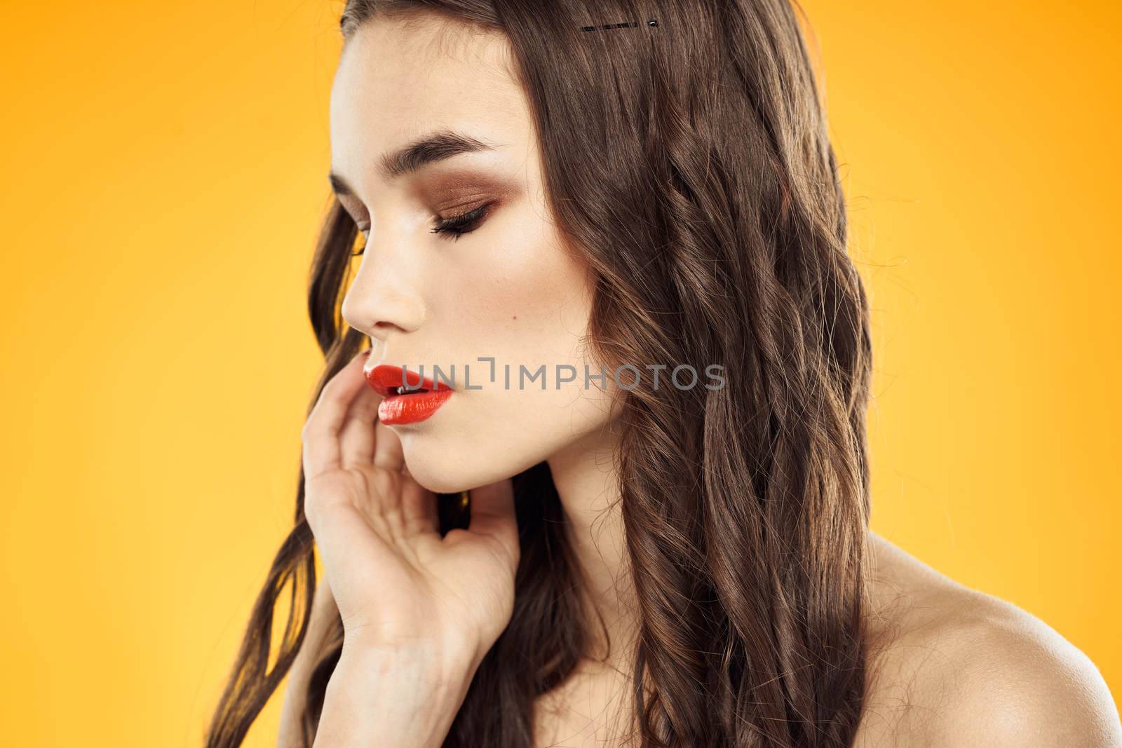 Beautiful brunette naked shoulders bright makeup red lips hairstyle close-up yellow background. High quality photo