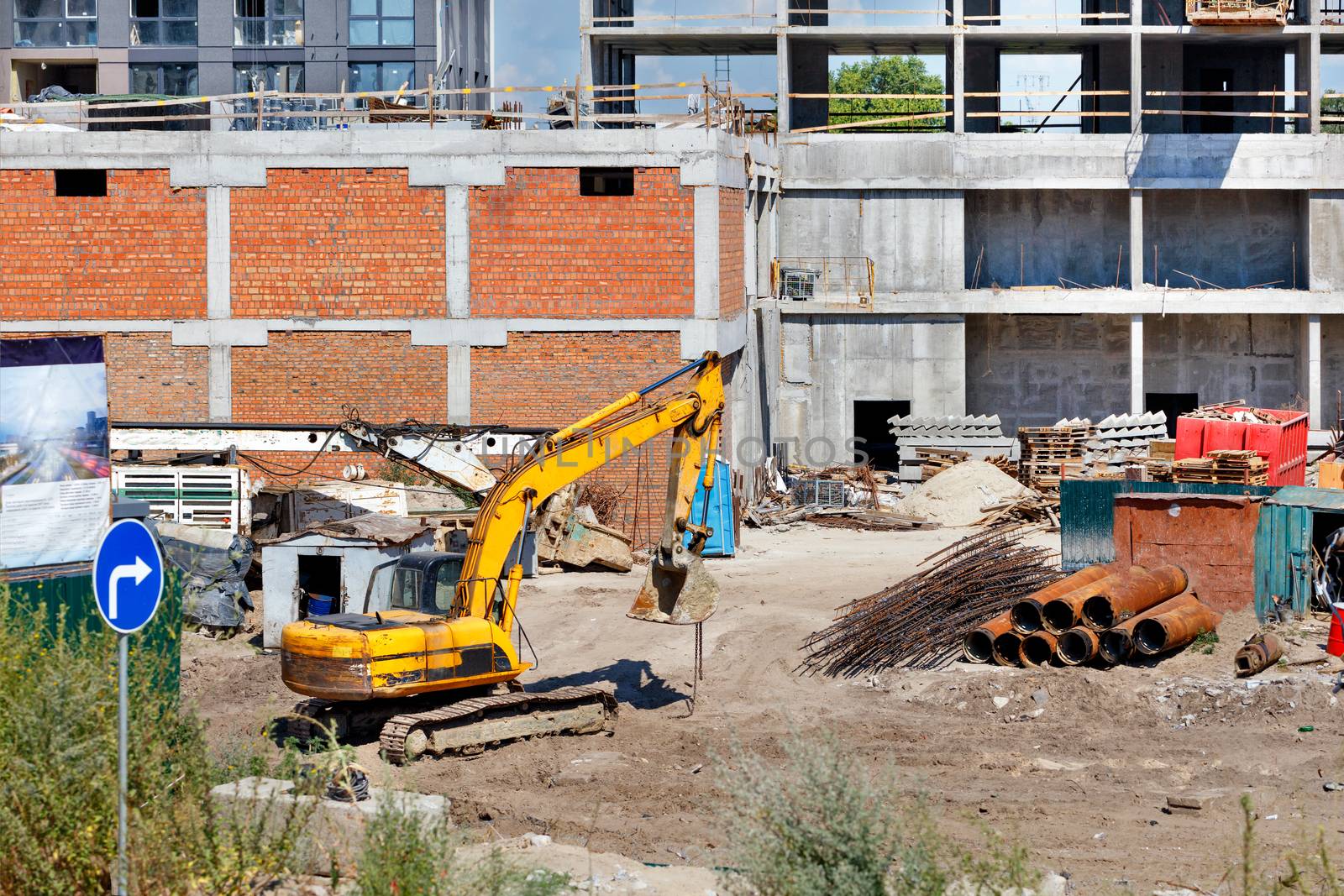 Heavy crawler construction excavator at a construction site during the construction of a residential building on a city street on a summer day.