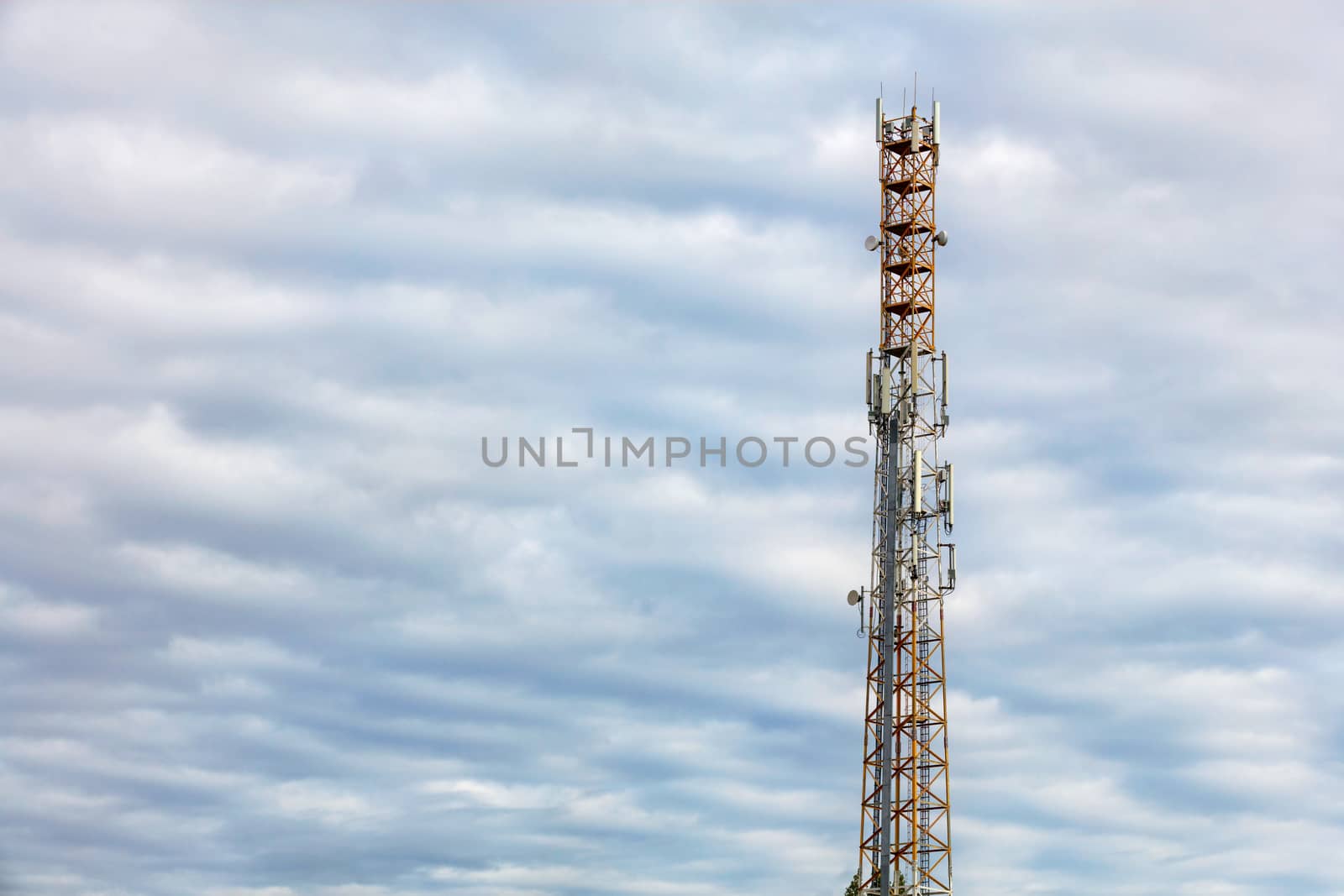 High telecommunication tower of 3G, 4G and 5G cellular communication with antennas against blue cloudy sky, copy space.