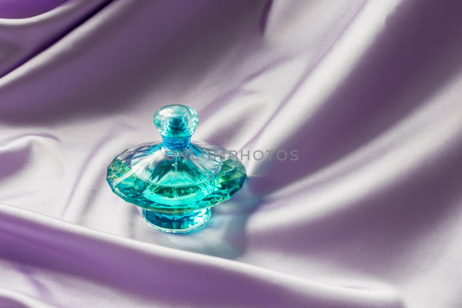 Perfume bottle on lilac silk folded fabric background. by galinasharapova