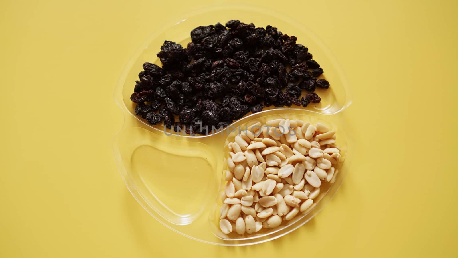 Dry fruits and nuts in round plastic container for food storage - yellow background. One container is empty