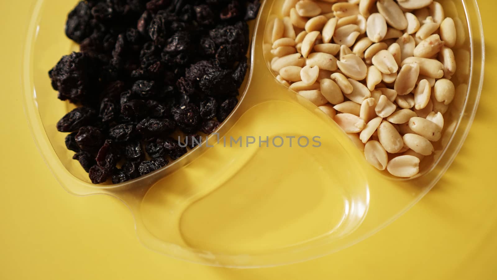 Dry fruits and nuts in round plastic container for food storage - yellow background. One container is empty