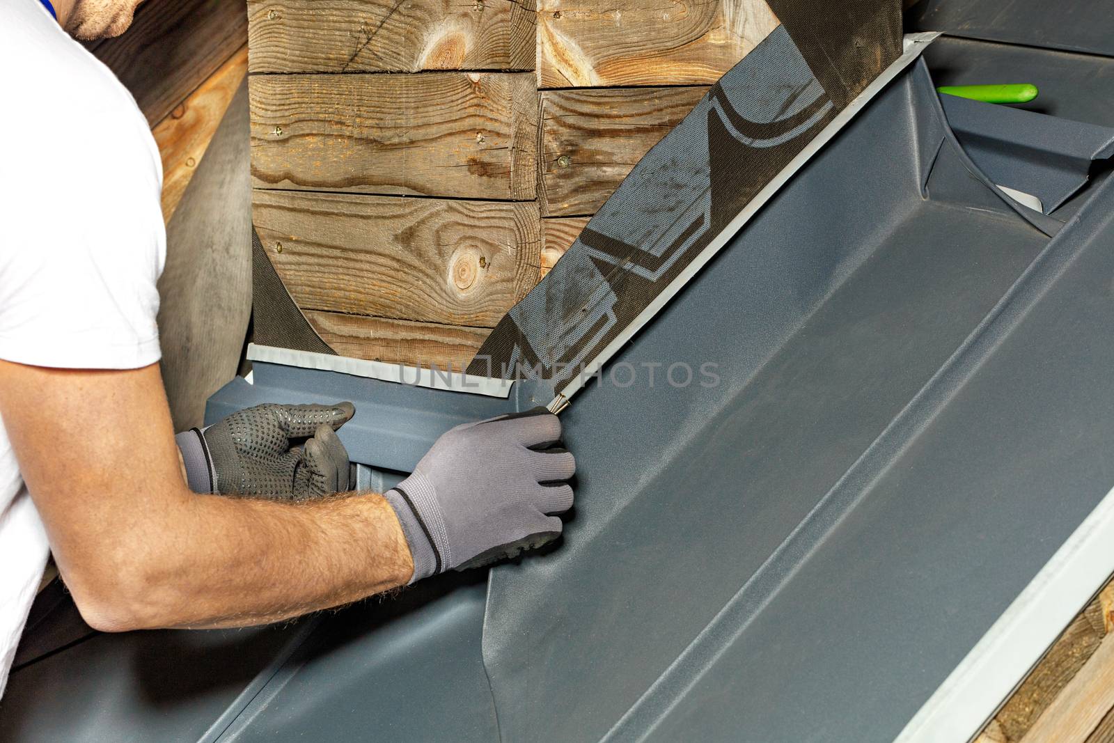 A man uses screws to attach a special waterproof bitumen membrane to waterproof the chimney on the roof. Hands of an experienced contractor working on the roof, close up.