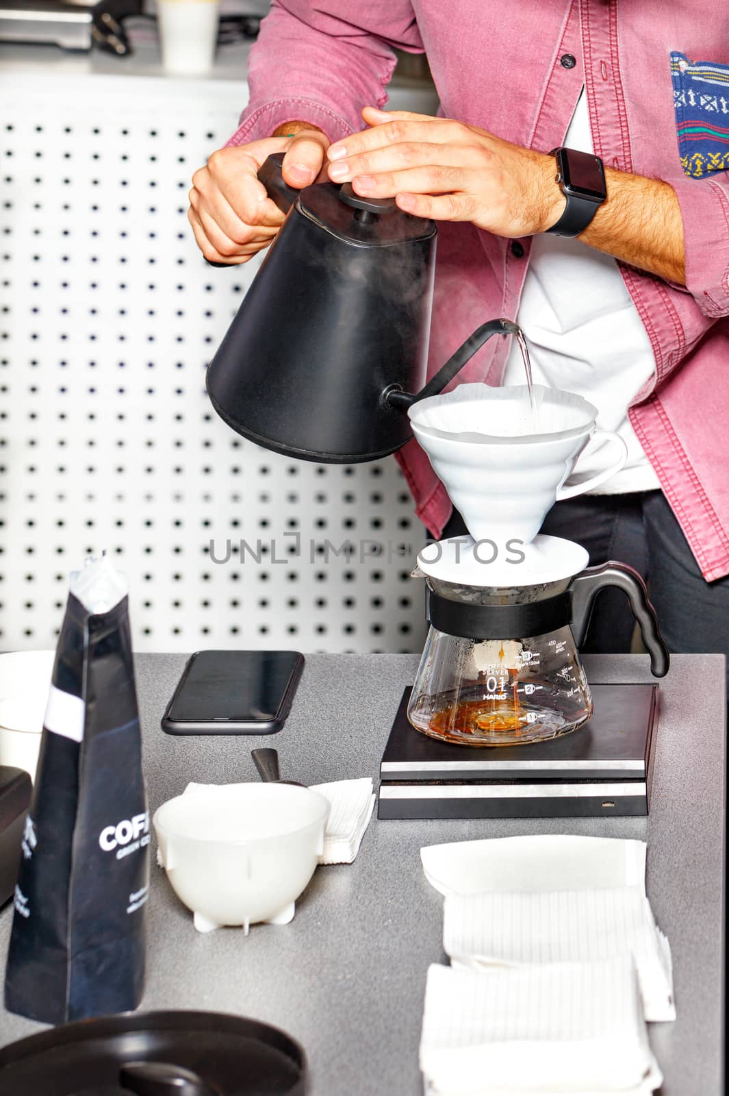 The barista's hands are preparing coffee by pouring boiling water into a white funnel. by Sergii