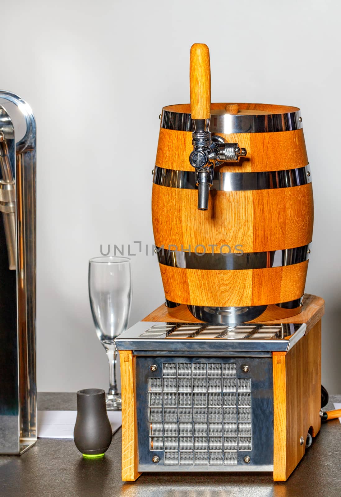 A new clean oak wooden barrel on the counter with a glass wine glass in the background.