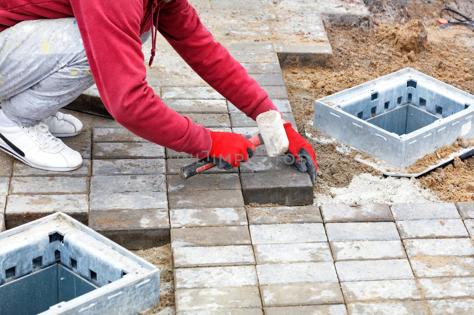 A worker lays paving slabs on the sidewalk around the utility shafts. by Sergii