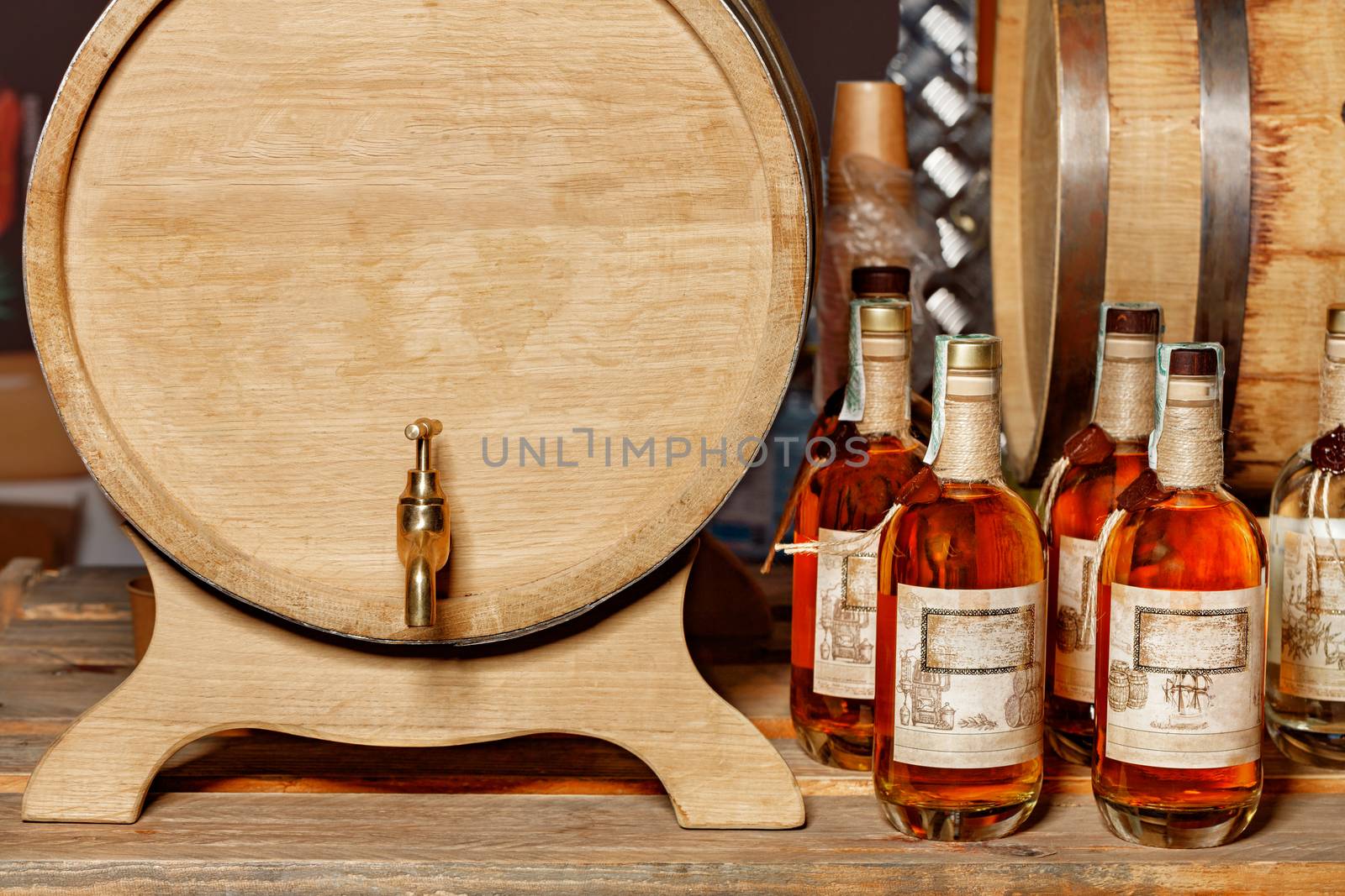 Front view of an oak barrel with a brass tap and sealed liquor bottles. The drinks are prepared according to old classic recipes, copy space.