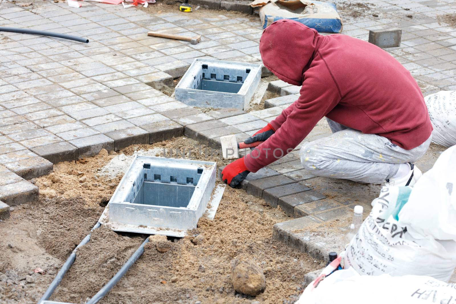 A worker installs utility shafts and lays paving slabs around them. by Sergii