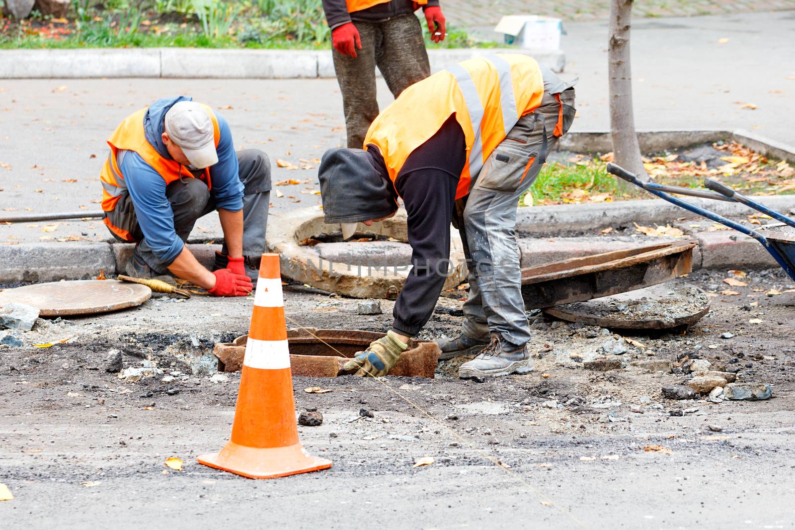 A team of road workers are replacing the old sewerage manhole with a new one. by Sergii