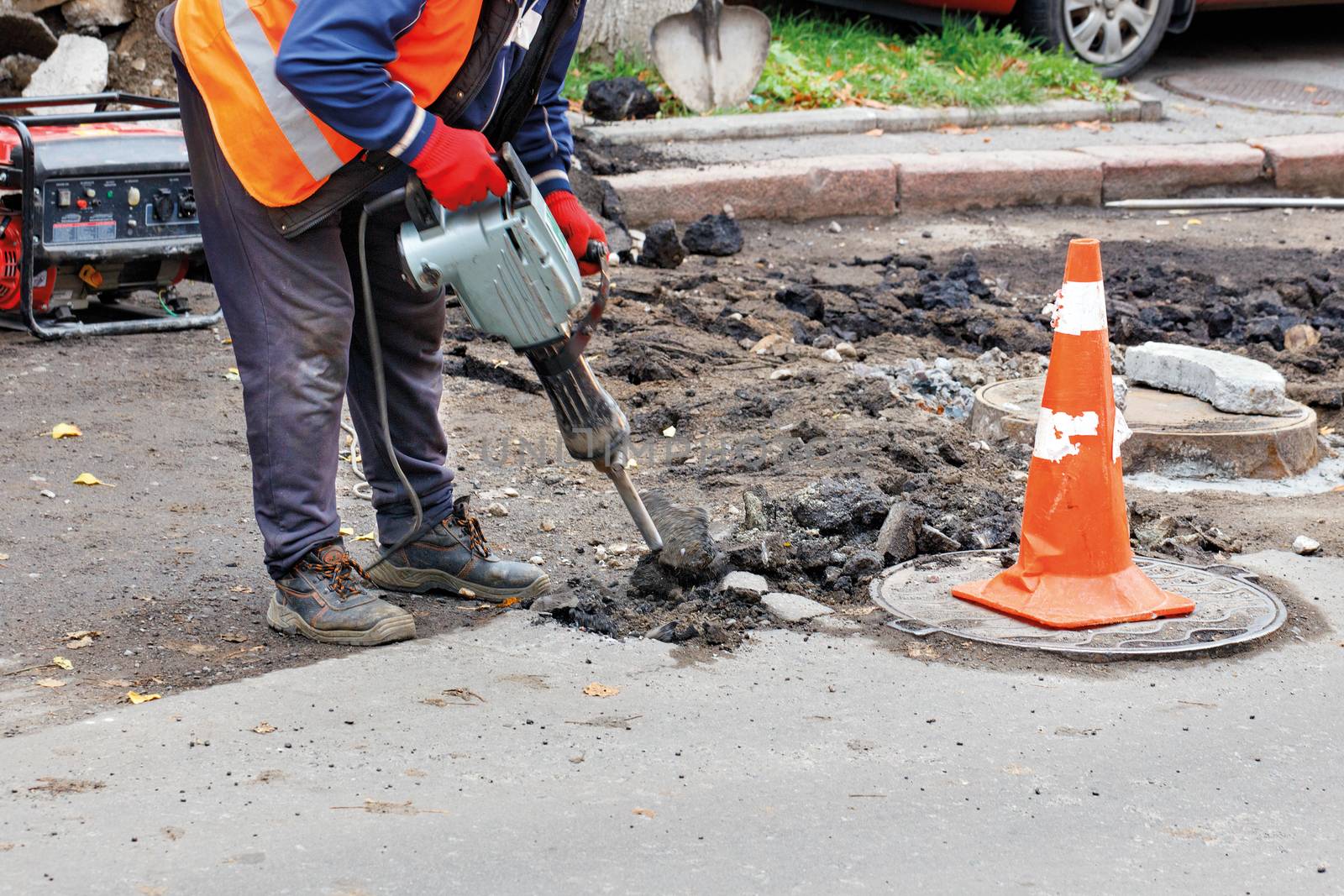 A road worker in reflective clothing breaks old asphalt off the road with an electric jackhammer.