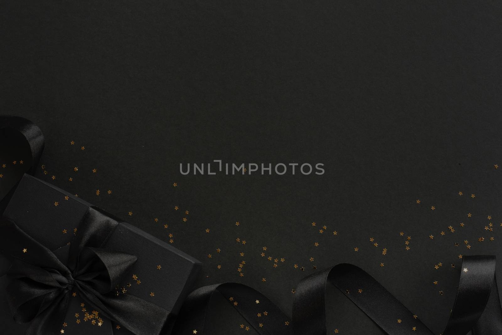 Black friday gift, paper box with silk ribbon bow and golden glitter stars on black paper background with copy space for text, flat lay top view template