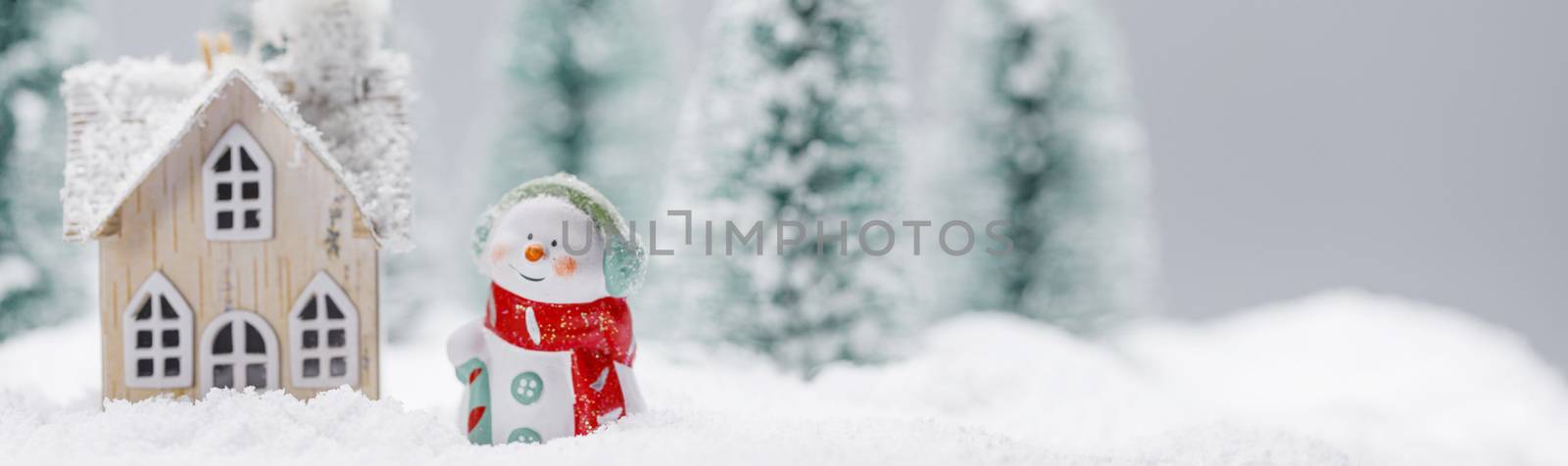 Small decorative snowman near wooden house in fir forest under falling snow