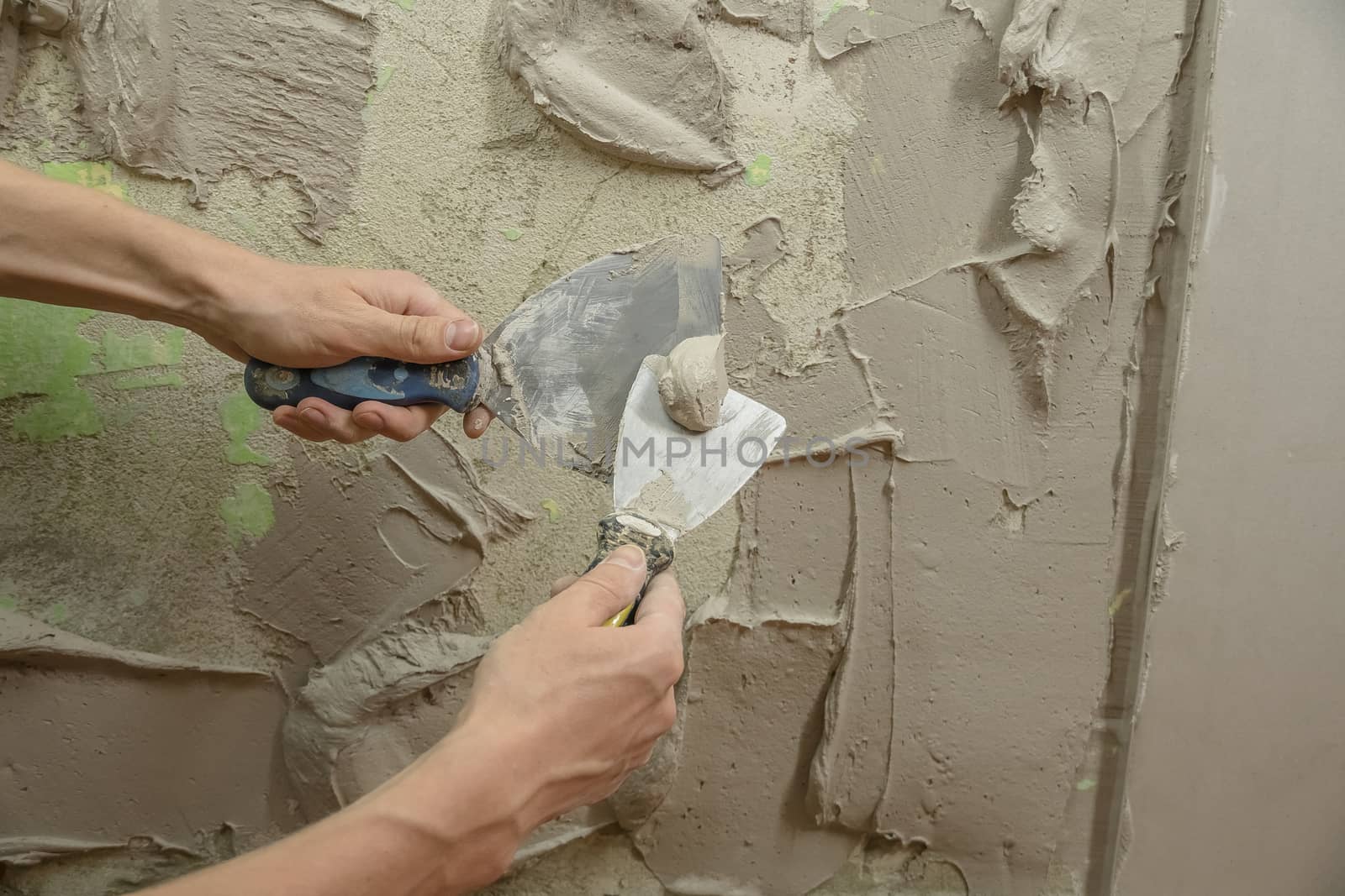 A worker plasters the wall with a spatula and applies a cement m by YevgeniySam