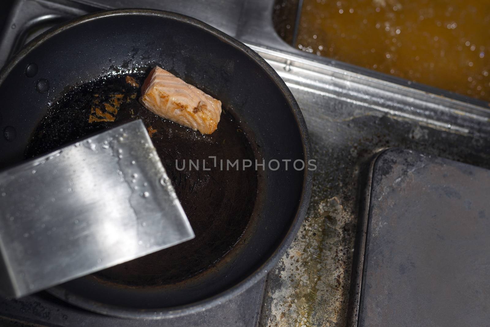 A piece of red fish in a black frying pan. Fried fish in the kitchen.