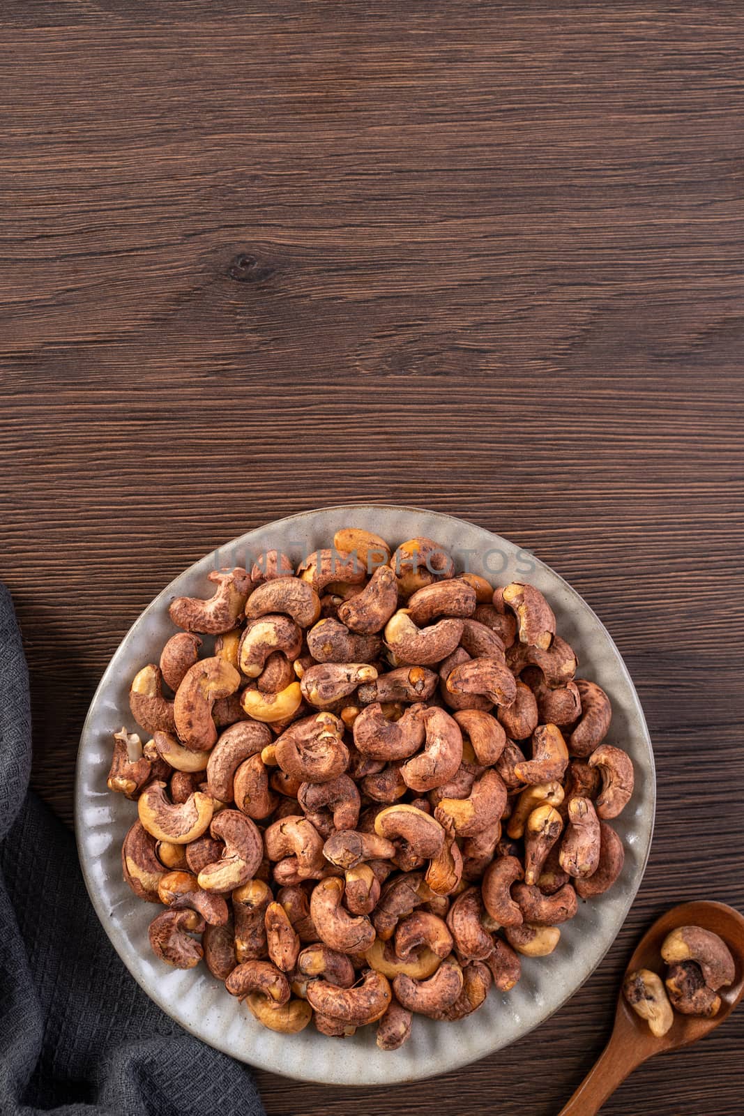 Cashew nuts with peel in a plate on wooden tray and table background, healthy raw food concept.