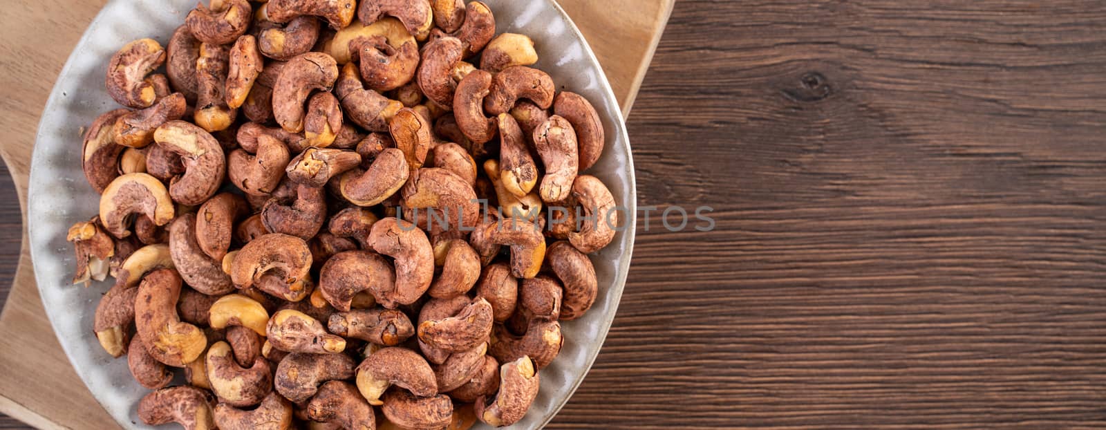 Cashew nuts with peel in a plate on wooden tray and table background, healthy raw food concept.