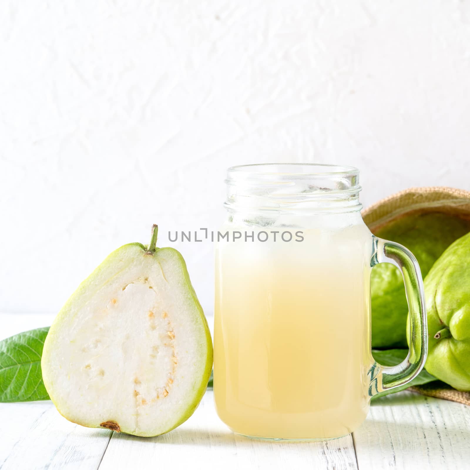 Delicious beautiful guava fruit with fresh juice set isolated on bright white wooden table background, close up.