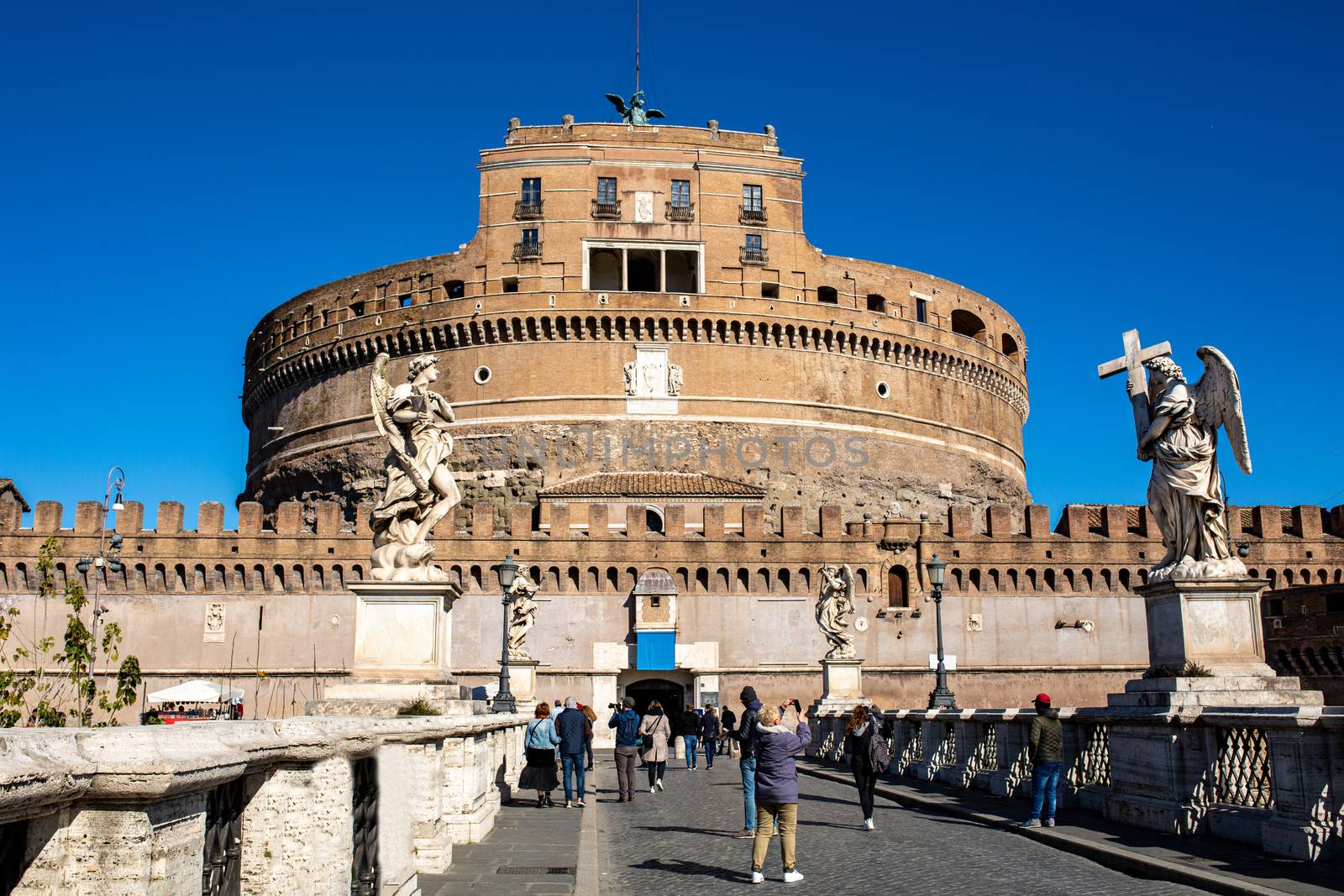 Frontal view of the Castel Sant'Angelo against the blue sky in Rome, Italy. tourists walk on the bridge