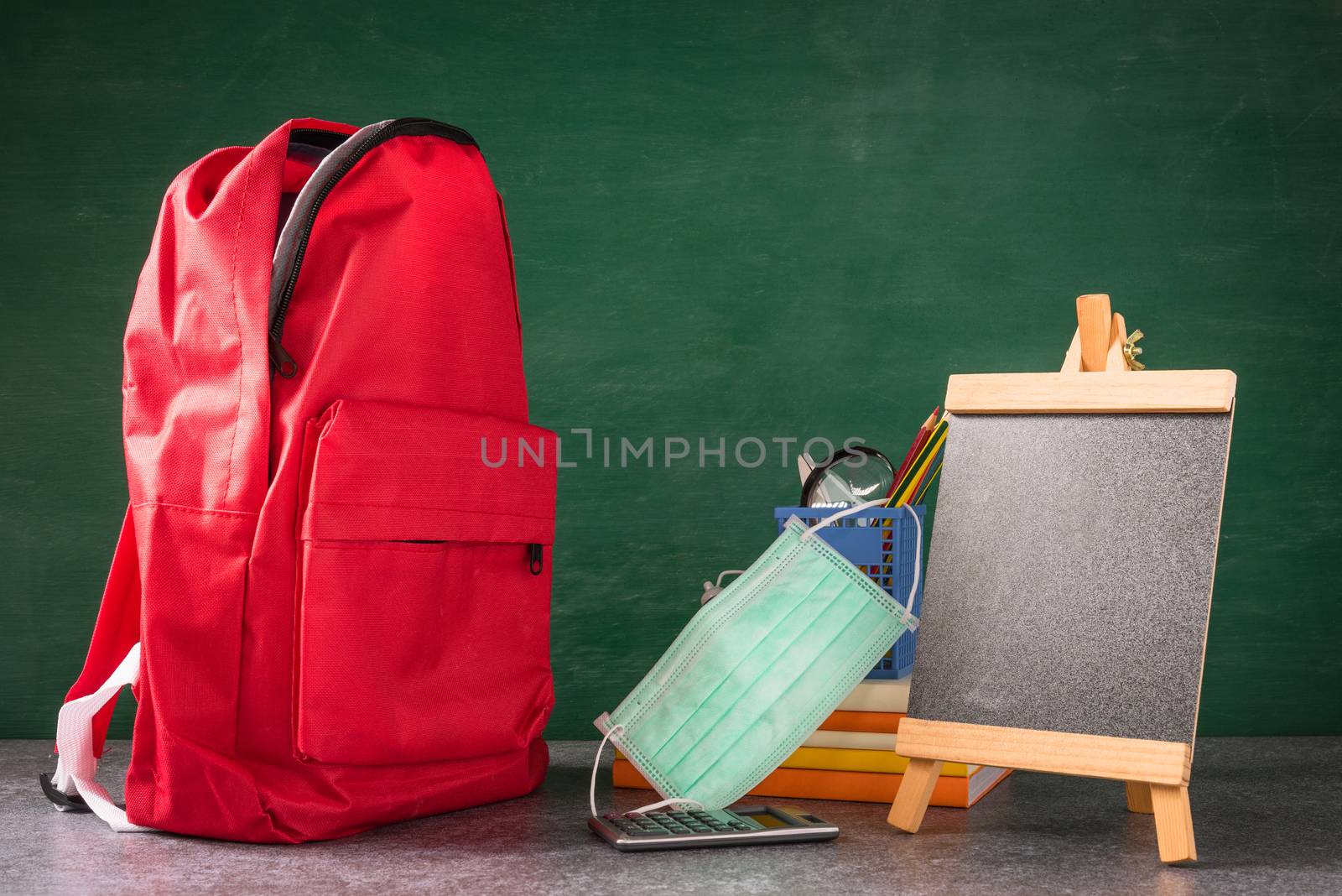 Front school backpack and accessories with face mask protect on desk at green chalkboard, student bag at classroom backboard, Back to school education new normal outbreak COVID-19 or coronavirus