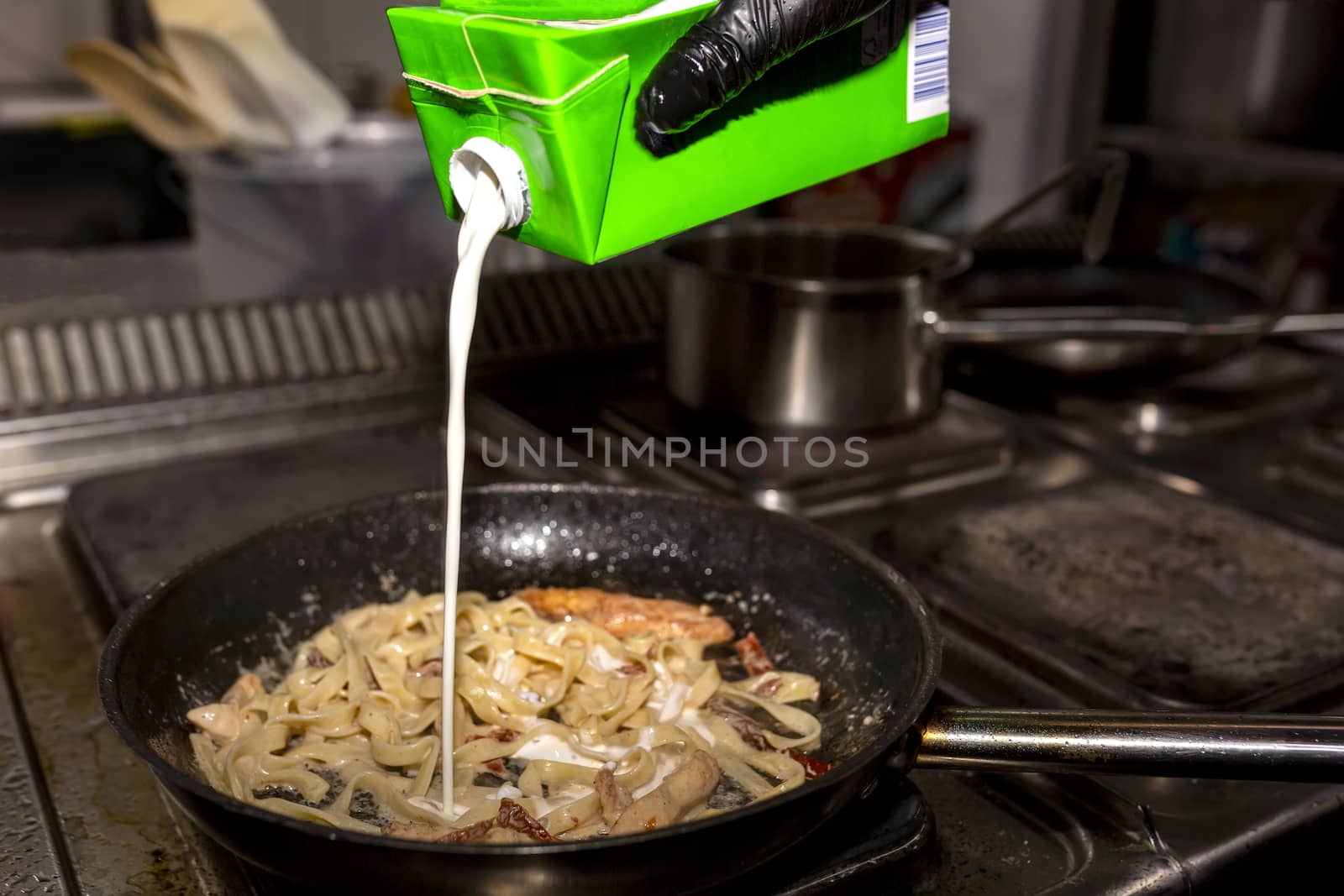 The cook adds cream to the pasta, which he warms in a black pan by 977_ReX_977
