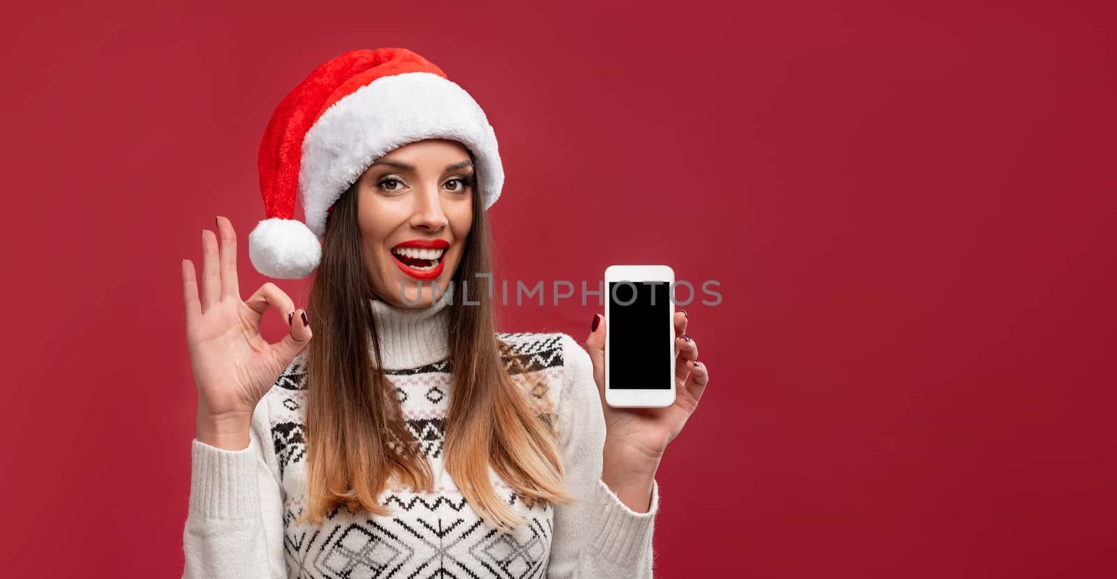 Close up portrait beautifiul caucasian woman in red Santa hat on red studio background. Christmas New Year holiday concept. Cute girl teeth smiling positive emotions with free copy space