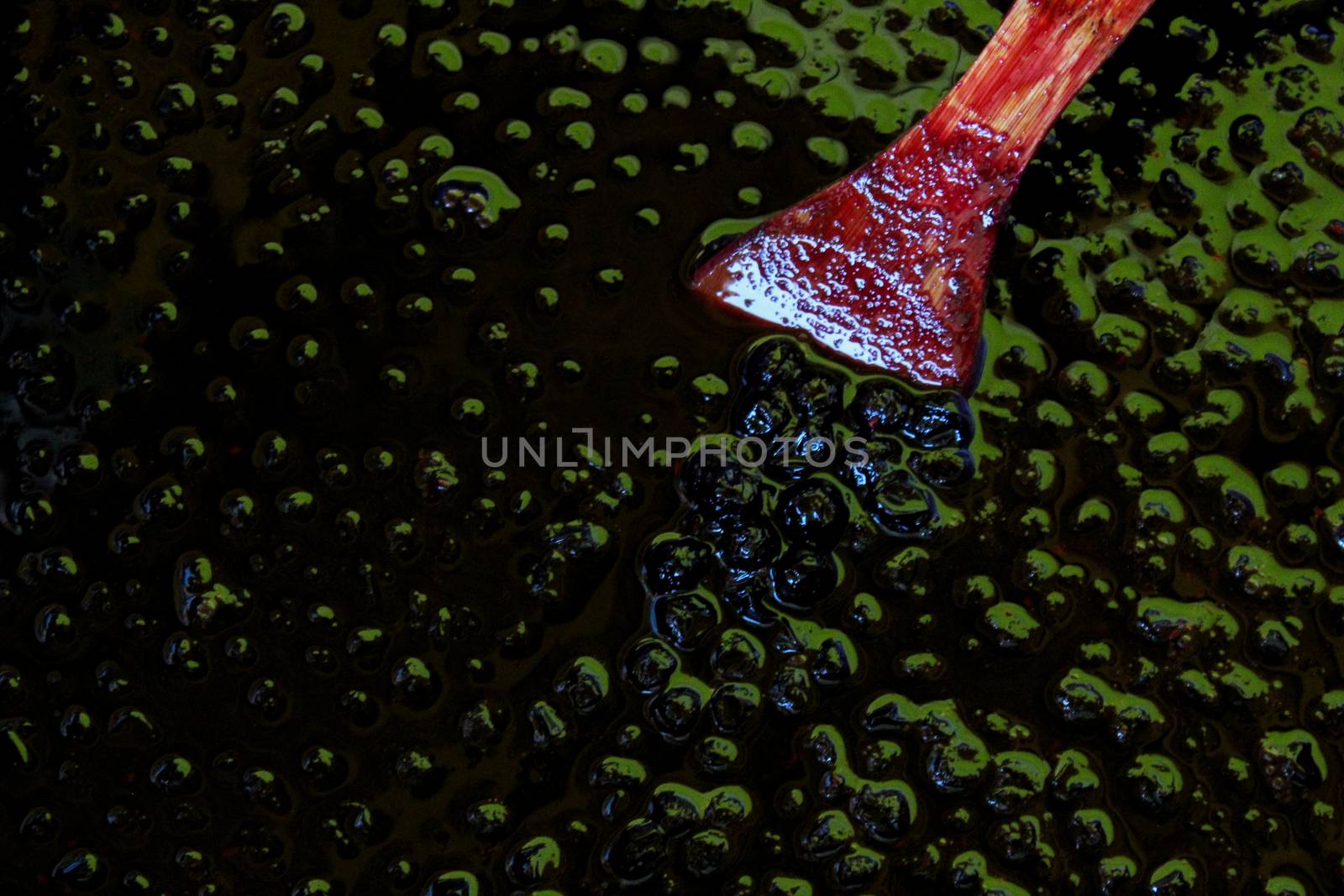 Top down view of chokeberry jam, on the surface of the berries with a wooden cooking spoon. by mahirrov