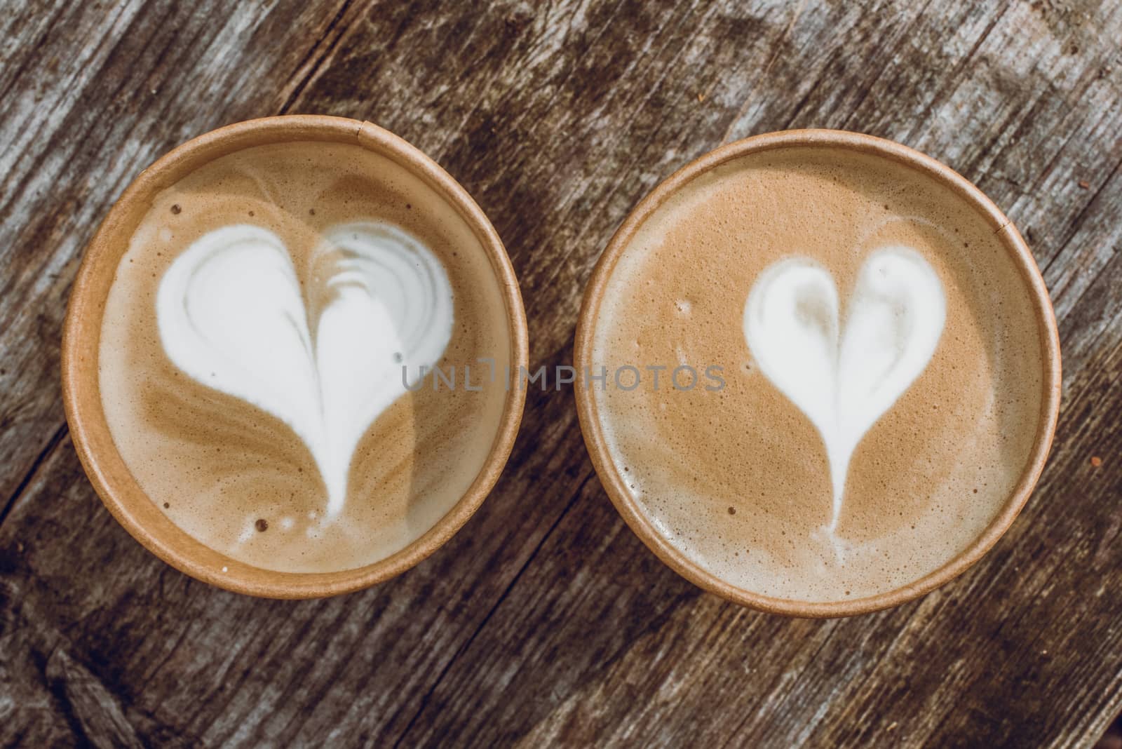 Two paper cups of coffee with heart shape latte art on wooden background on Valentine Day