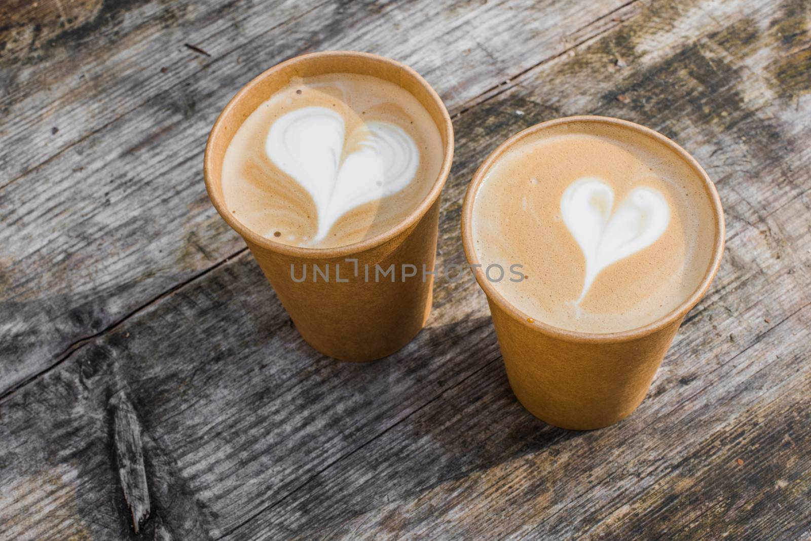 Two paper cups of coffee with heart shape latte art on yellow background