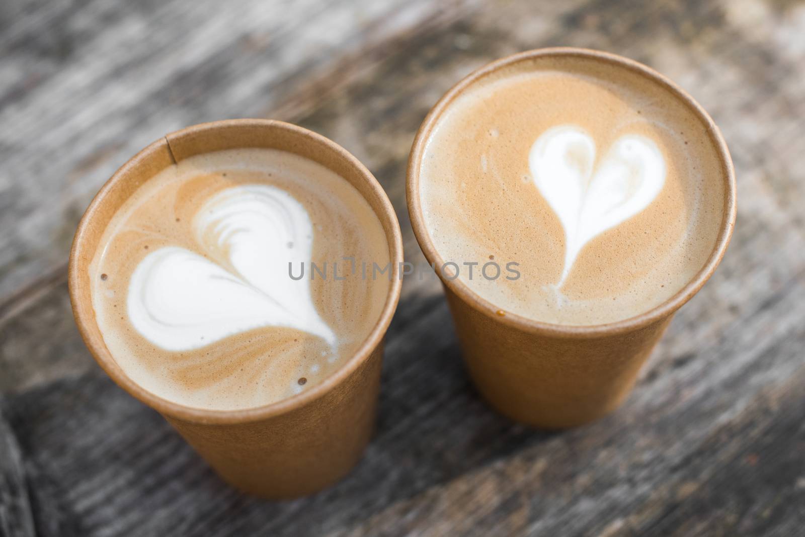 Two paper cups of coffee with heart shape latte art on yellow background