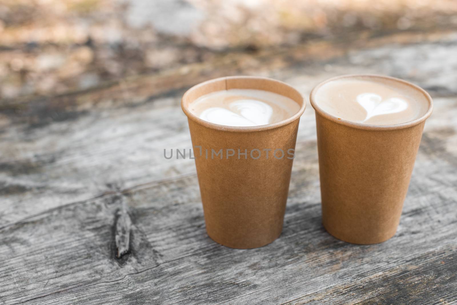 Two paper cups of coffee with heart shape latte art on yellow background