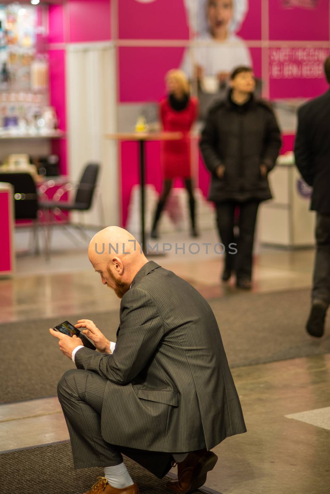 Young business (shaved head with bear) man checking his phone while attending an event at the convention trade center in Brno. BVV Brno Exhibition center. Czech Republic