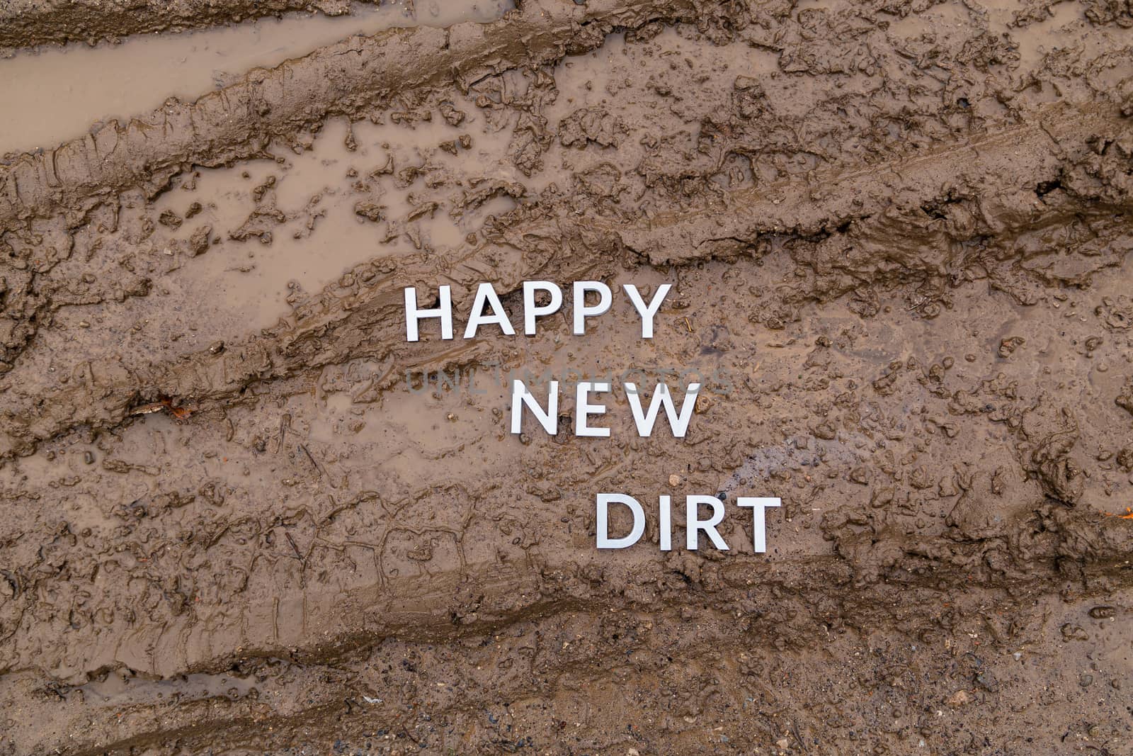 the words happy new dirt laid with silver metal letters on wet mud surface in directly above perspective under cloudy autumn day light