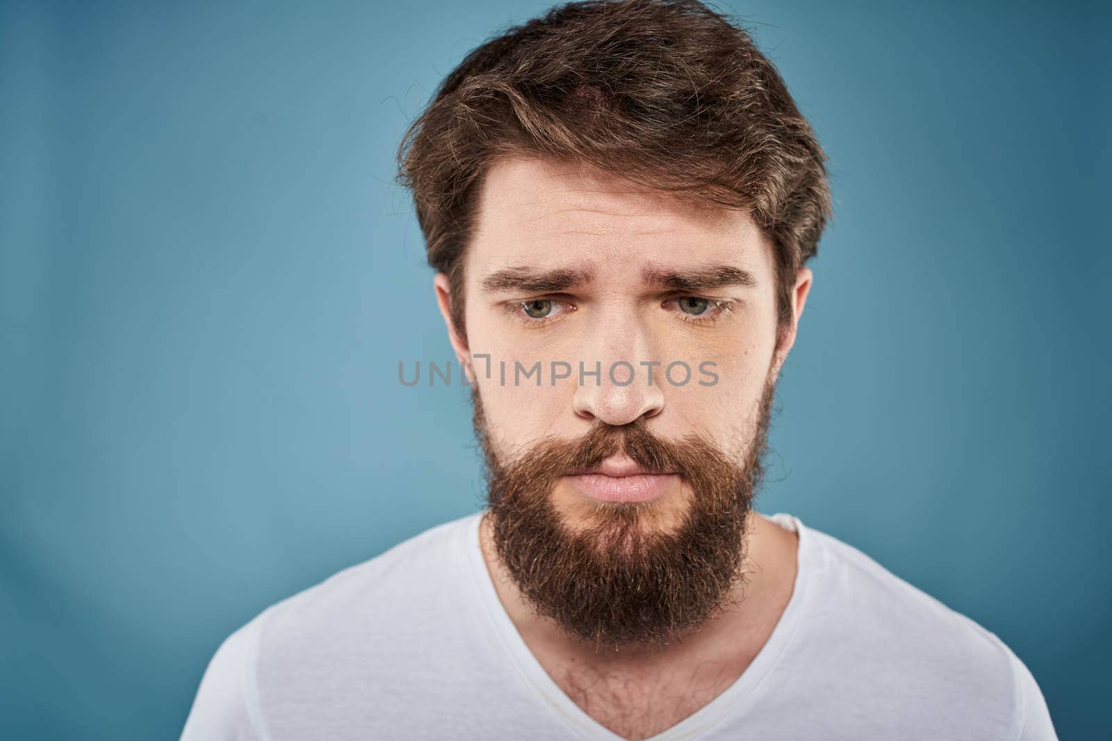 Bearded man displeased facial expression emotions close-up blue background white t-shirt. High quality photo