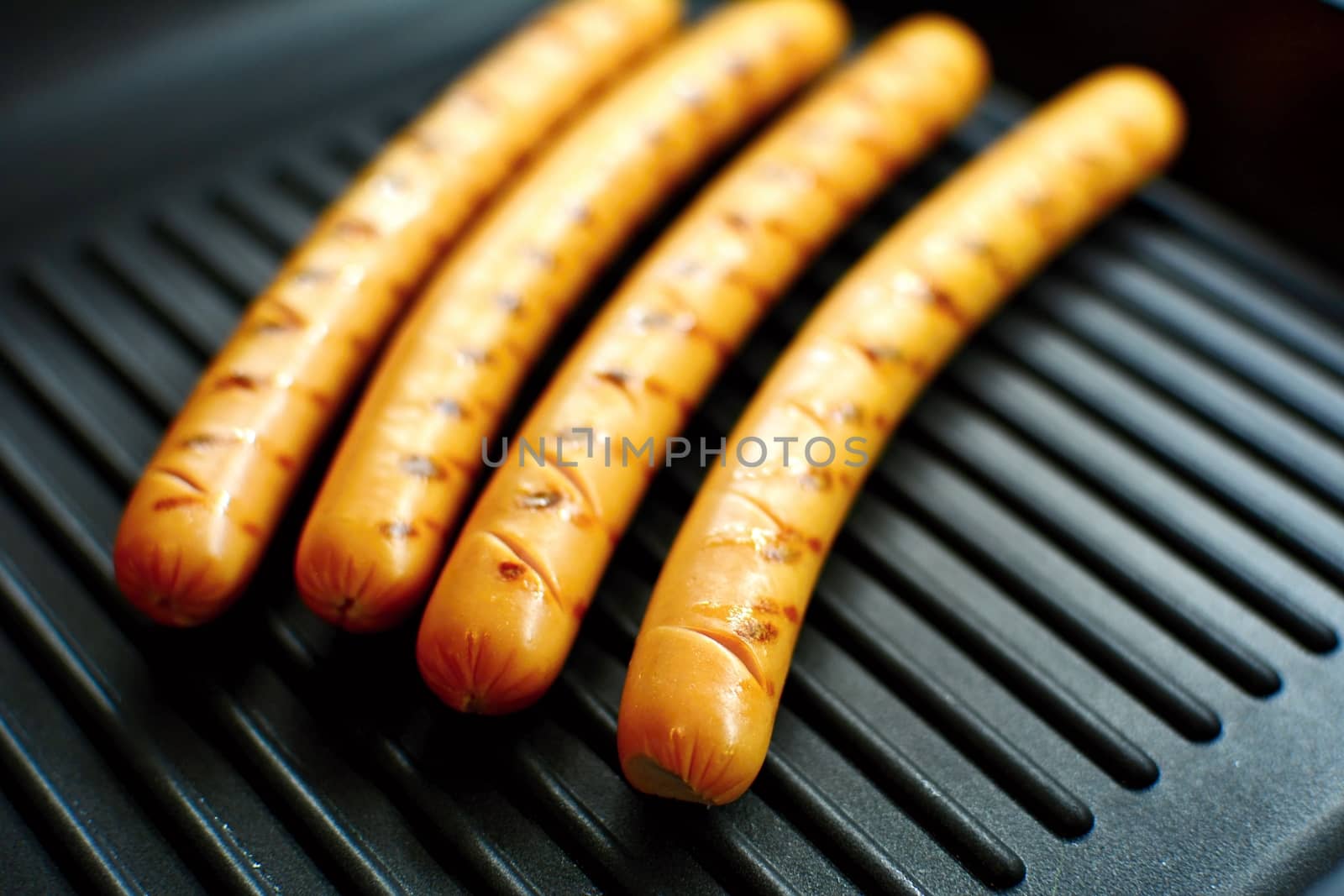 Closeup of a four sausages on a black grill pan.