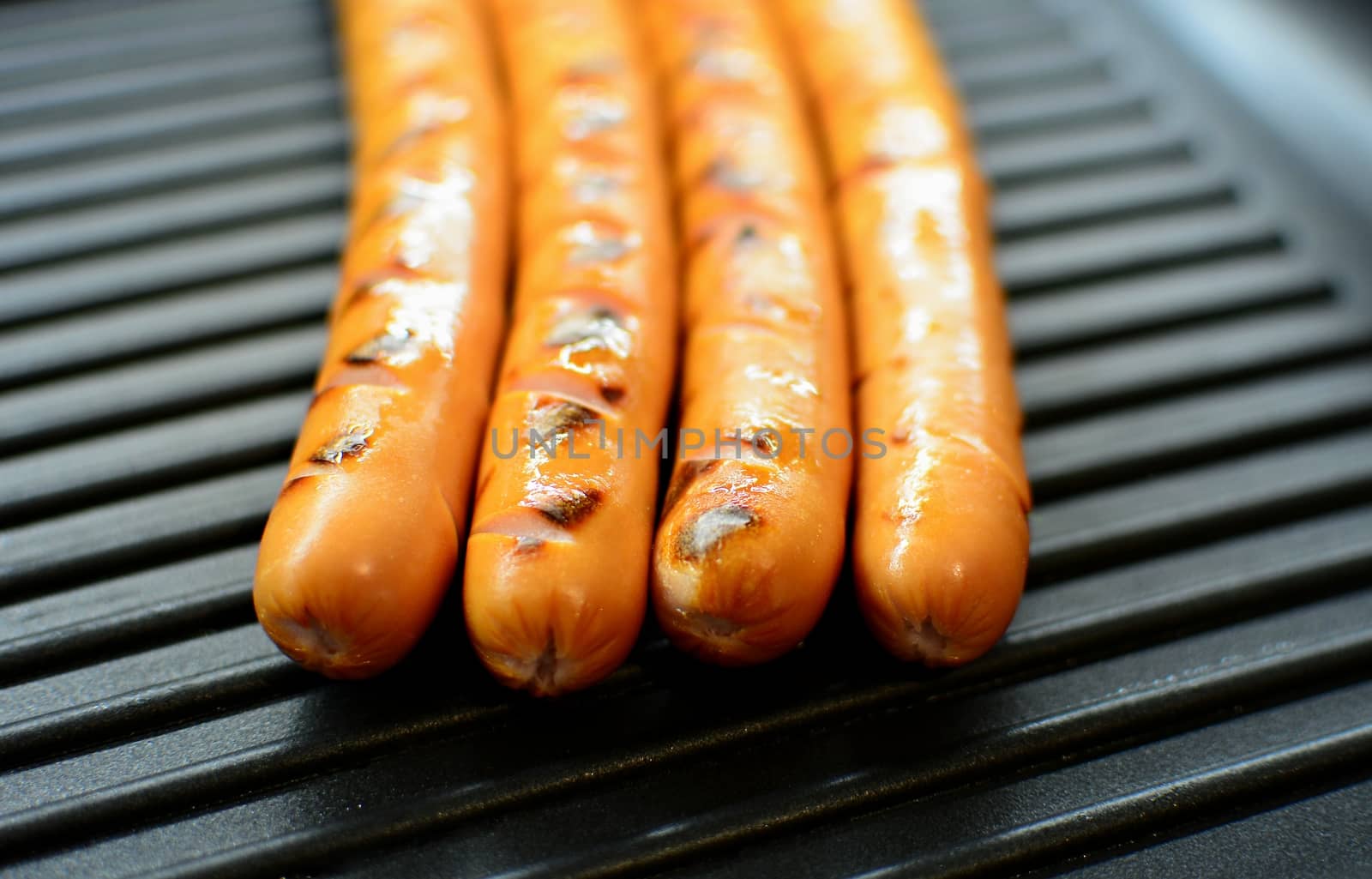 Closeup of a four sausages on a black grill pan.