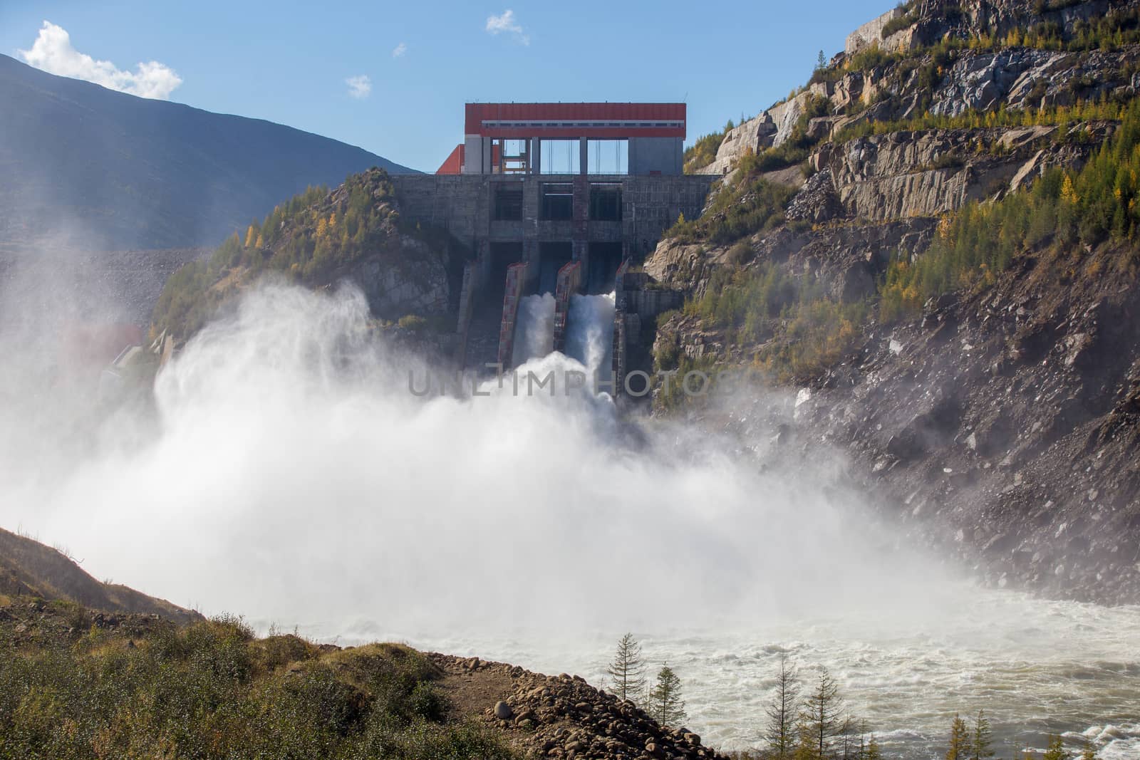 Kolyma hydroelectric power station in Magadan region, Russia. Spillway from the dam of the hydroelectric power station. A huge stream of water flows into the river against the background of high hills by PrimDiscovery