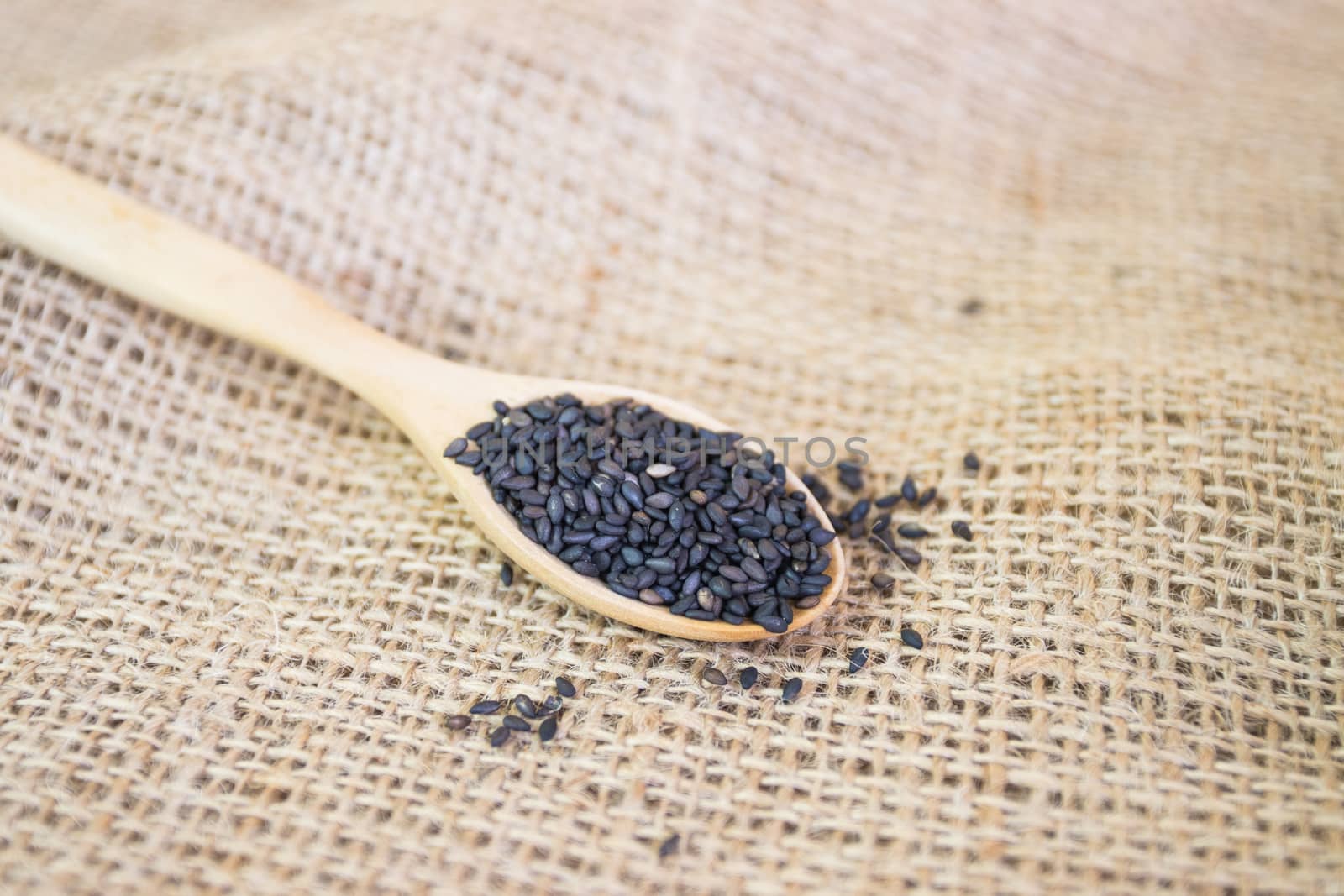 Black sesame seeds in wooden spoon pile  