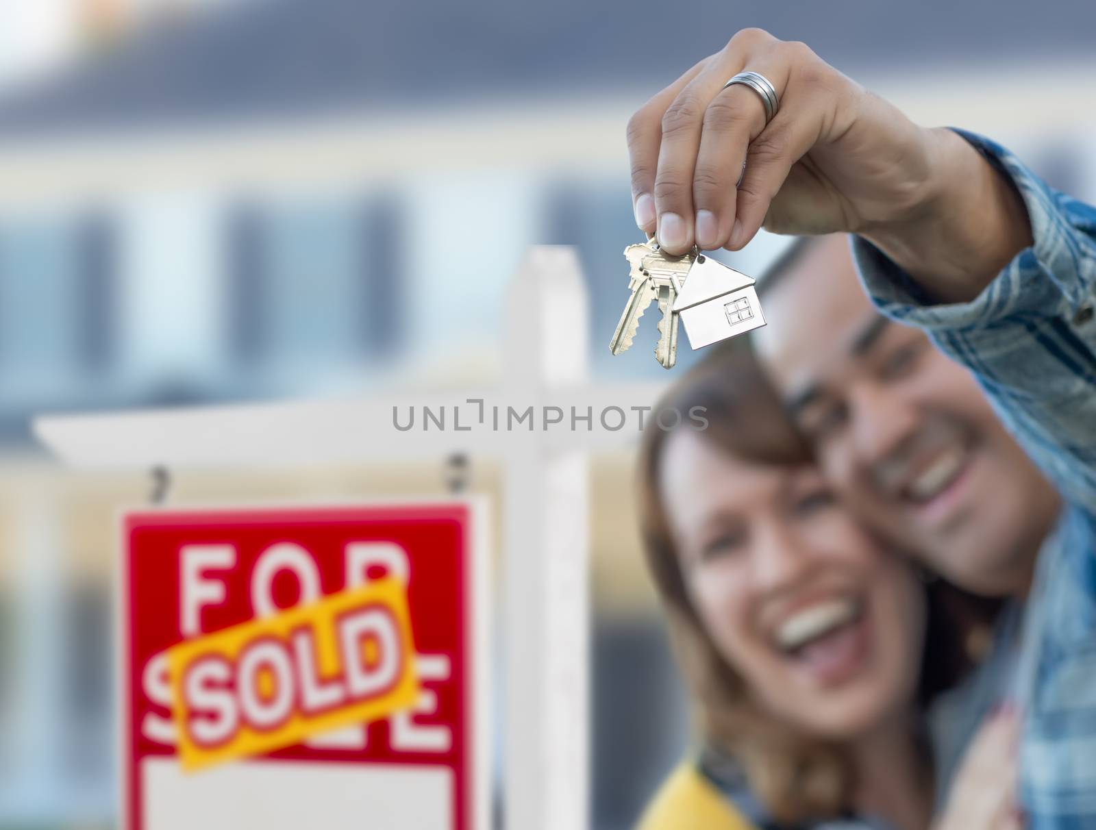 Mixed Race Couple in Front of Sold Real Estate Sign and House with Keys.