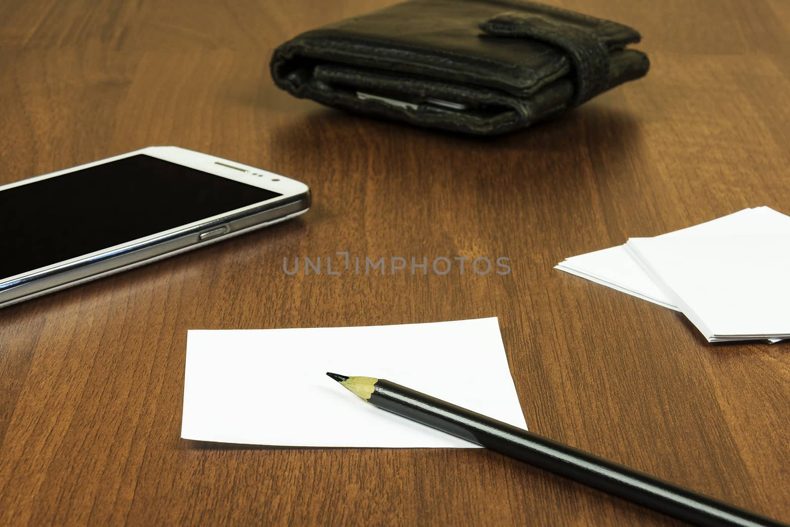 On the surface of the table lie a sheet for notes, a pencil, a smartphone and a purse