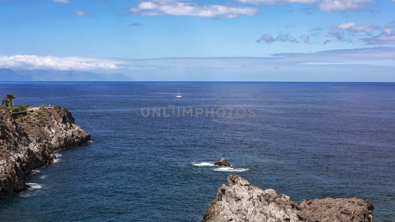 Seascape. A sailboat with white sails floats along the rocky coast of Los Gigantos (Tenerife, Spain)
