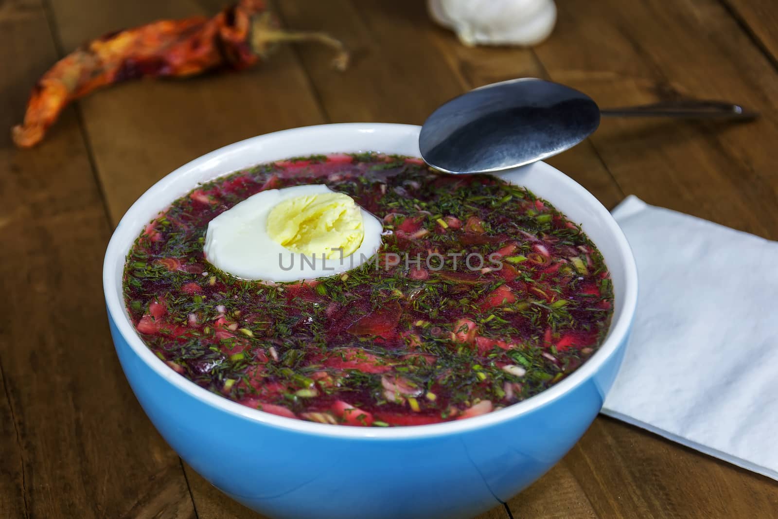 Cold soup with egg in a blue porcelain bowl is on a wooden table